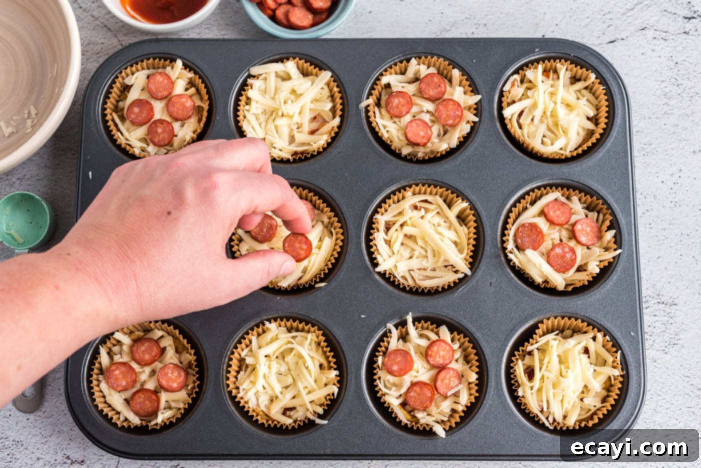 Cauliflower Crust Pizza Bites 9 hand adding mini pepperoni to cauliflower pizza bites in a muffin tin