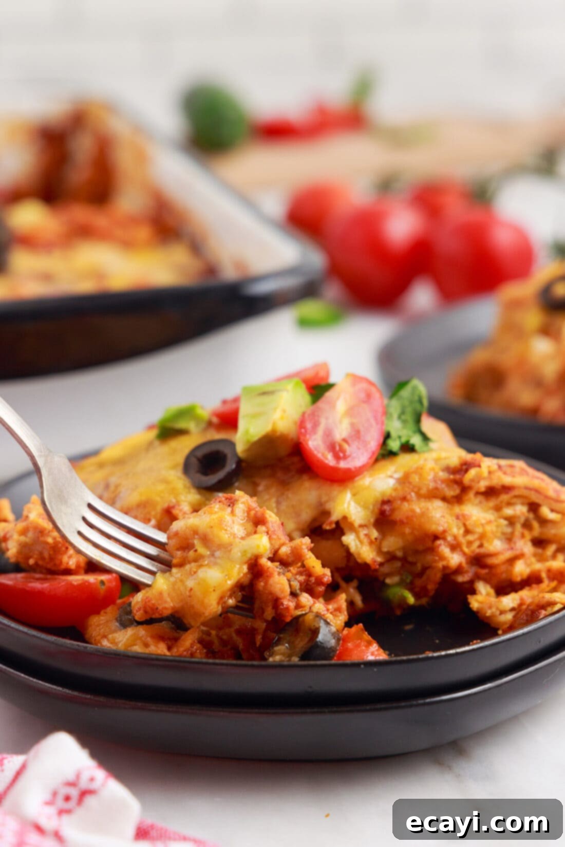 Cheesy Chicken Enchilada Bake 13 A close-up of a serving of Chicken Enchilada Casserole on a white plate with a fork.