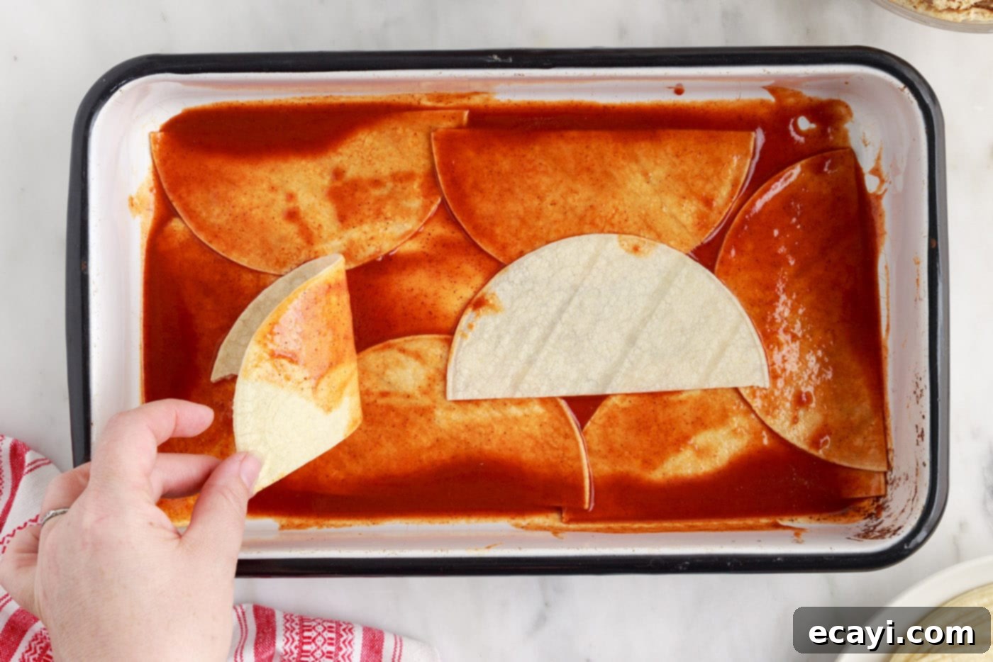 Cheesy Chicken Enchilada Bake 5 Dipping corn tortilla halves in red enchilada sauce before layering in a casserole dish.