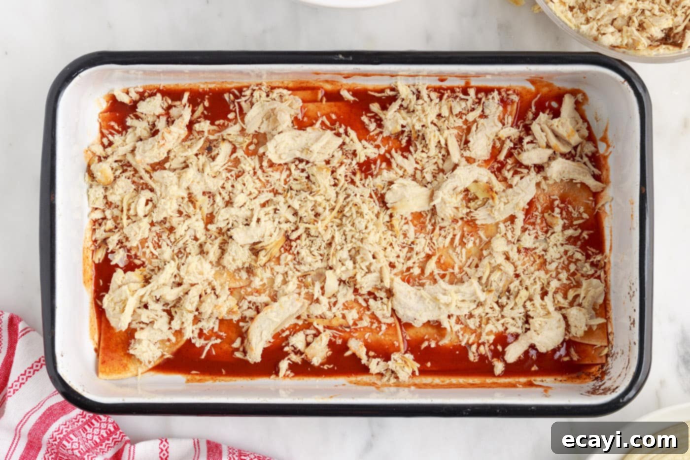 Cheesy Chicken Enchilada Bake 6 Layer of shredded chicken spread over tortillas and enchilada sauce in a baking dish.