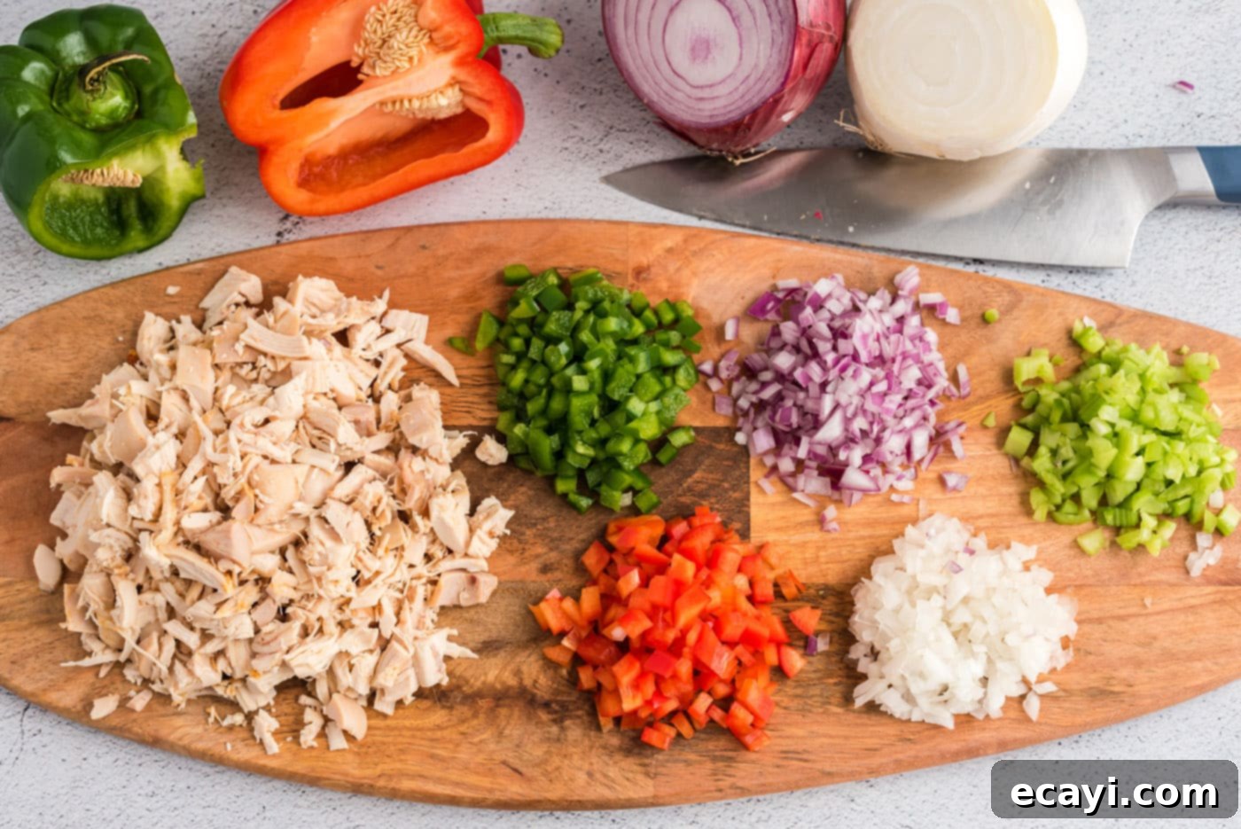 Bayou Chicken Salad 5 Close-up photo of various chopped vegetables including celery, red and white onions, and red and green bell peppers, alongside chunks of cooked chicken, all ready to be mixed on a clean cutting board.