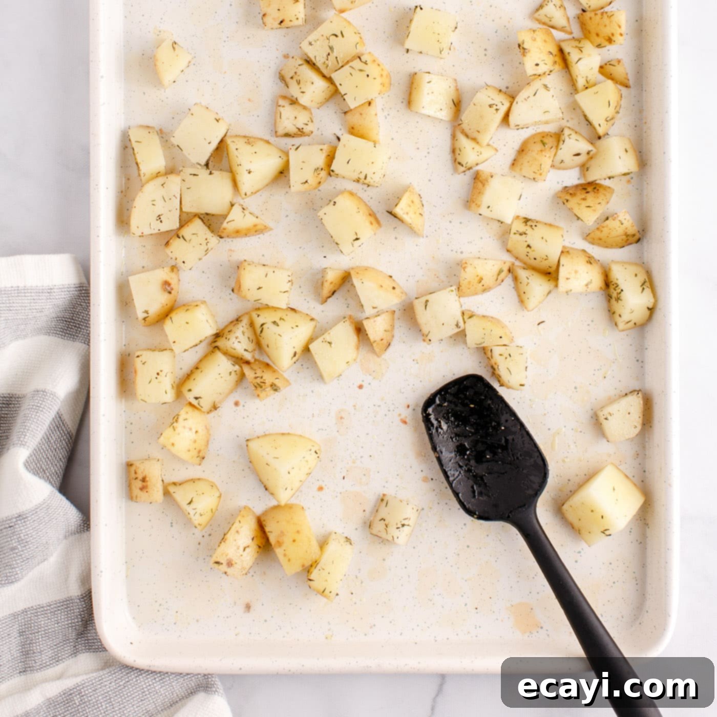Crispy Corned Beef Hash 6 Seasoned cubed potatoes spread in a single layer on a baking sheet, ready for oven roasting