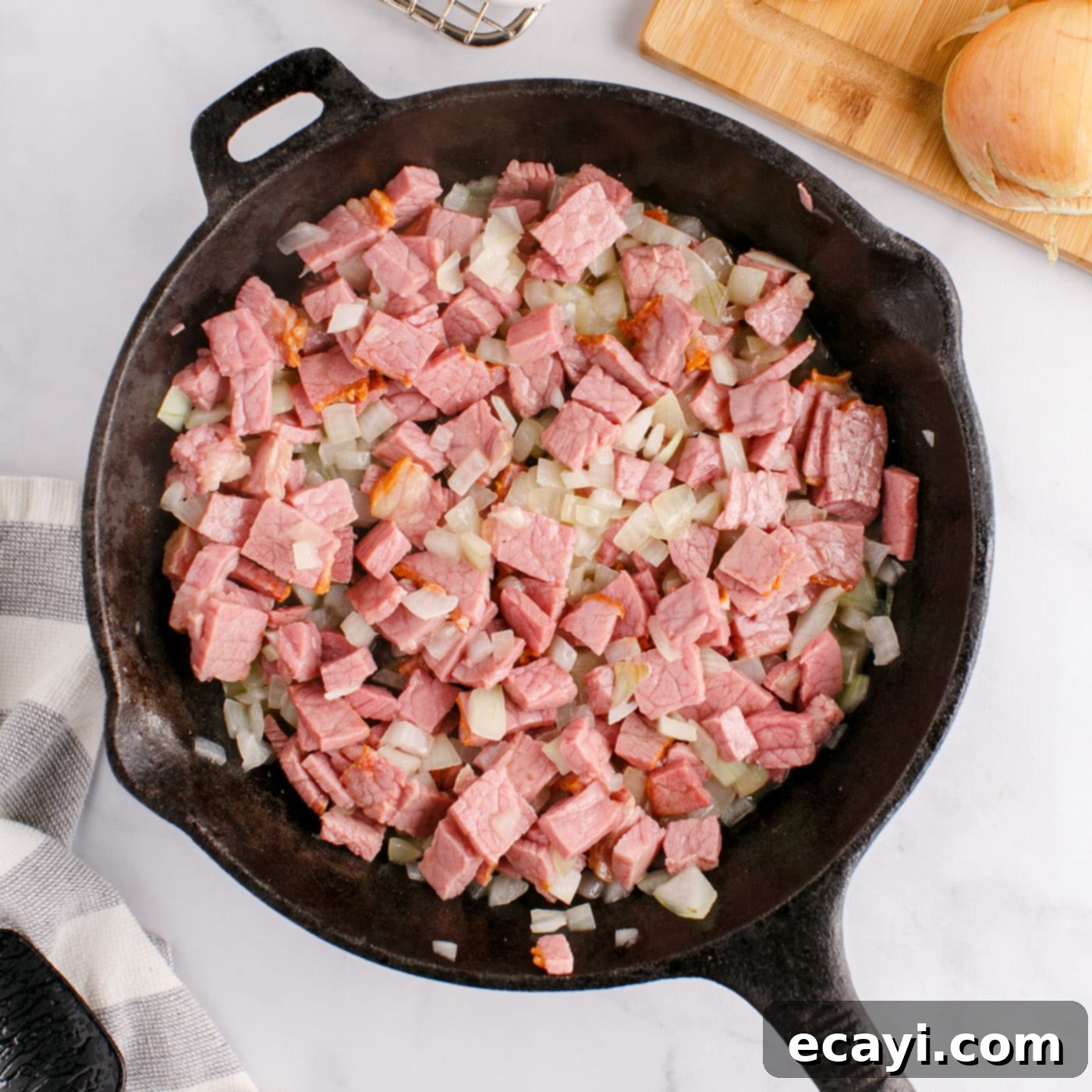 Crispy Corned Beef Hash 8 Cubed corned beef being cooked with sautéed onions in a cast iron skillet