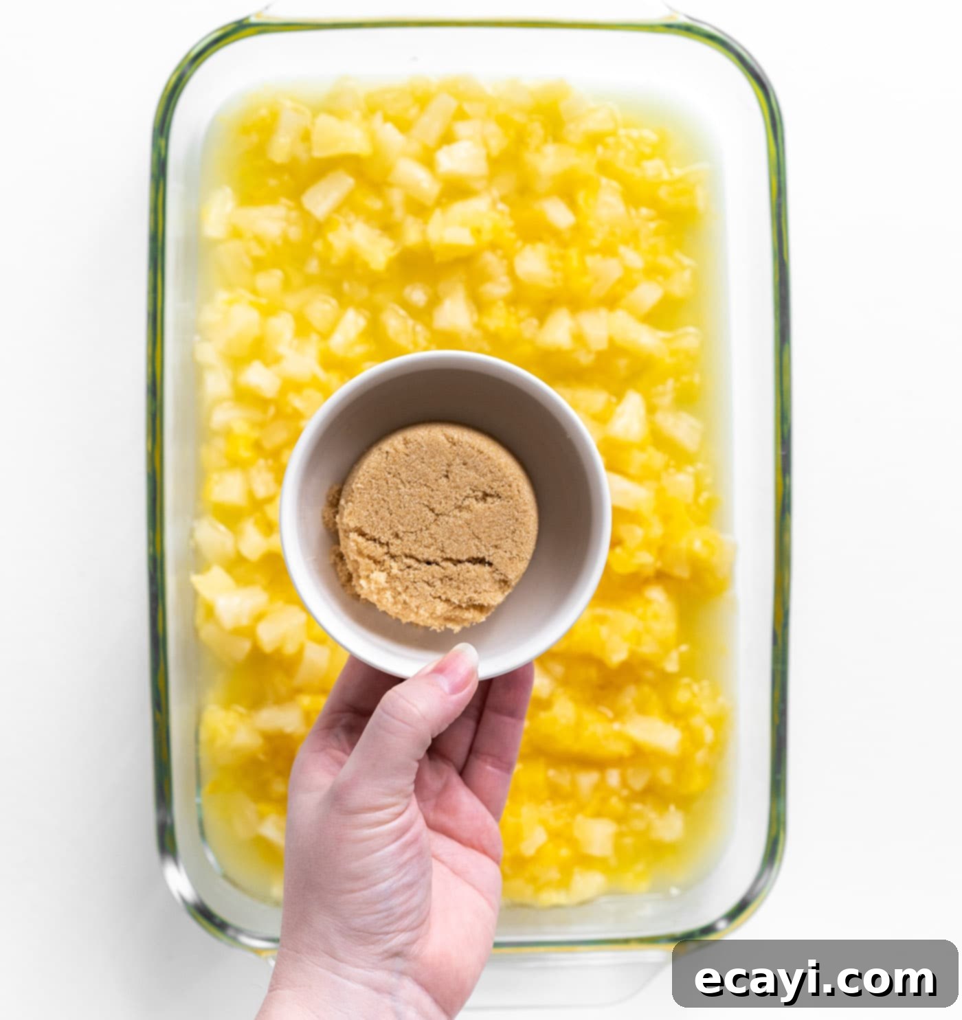 Easy Pineapple Cake 6 hand holding brown sugar over crushed pineapple in a baking dish