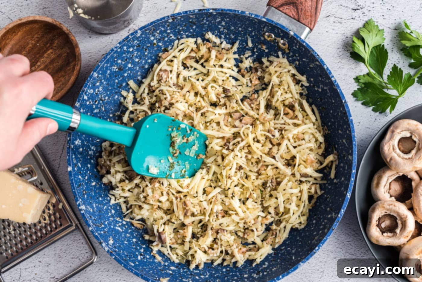 Gourmet Mushroom Poppers 7 A spatula stirring a creamy mixture of cheeses, sautéed onions, and herbs in a pan.