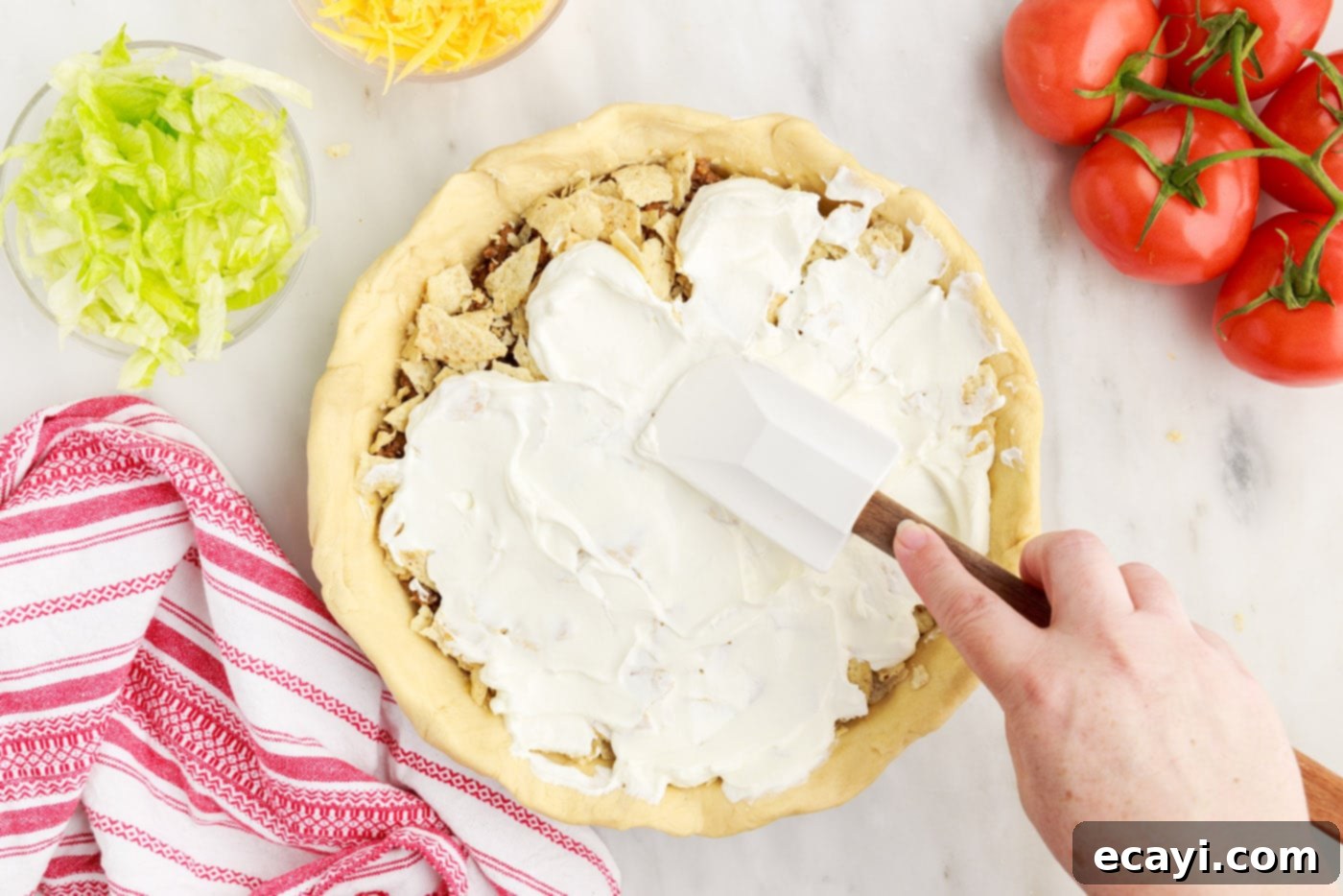 Ultimate Taco Casserole 11 spatula spreading sour cream over taco pie