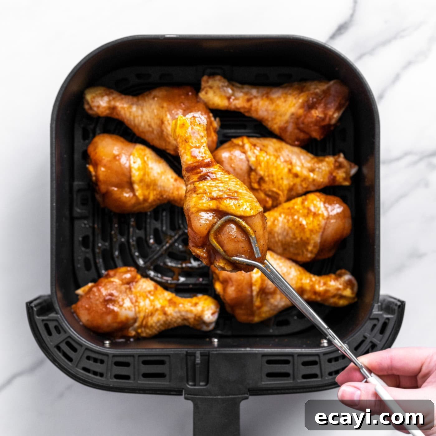 Golden Crispy Air Fryer Drumsticks 6 Tongs carefully placing a seasoned chicken drumstick into the preheated air fryer basket
