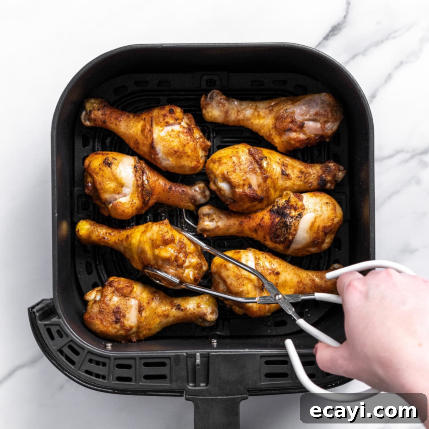 Golden Crispy Air Fryer Drumsticks 7 Tongs picking up a perfectly cooked, golden-brown chicken drumstick from the air fryer basket