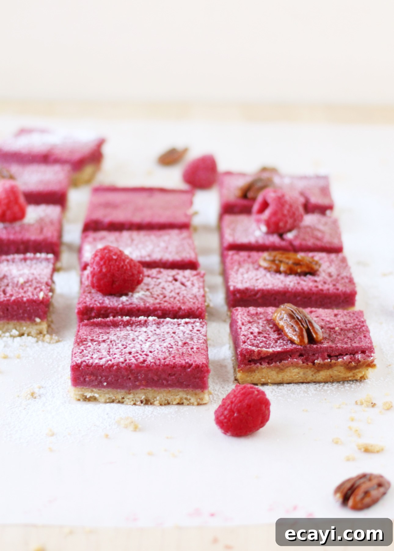 Luscious Raspberry Squares 2 Fresh Raspberry Squares: A close-up of vibrant red raspberry bars on a white surface, garnished with fresh raspberries and powdered sugar, showcasing their crisp crust and juicy filling.
