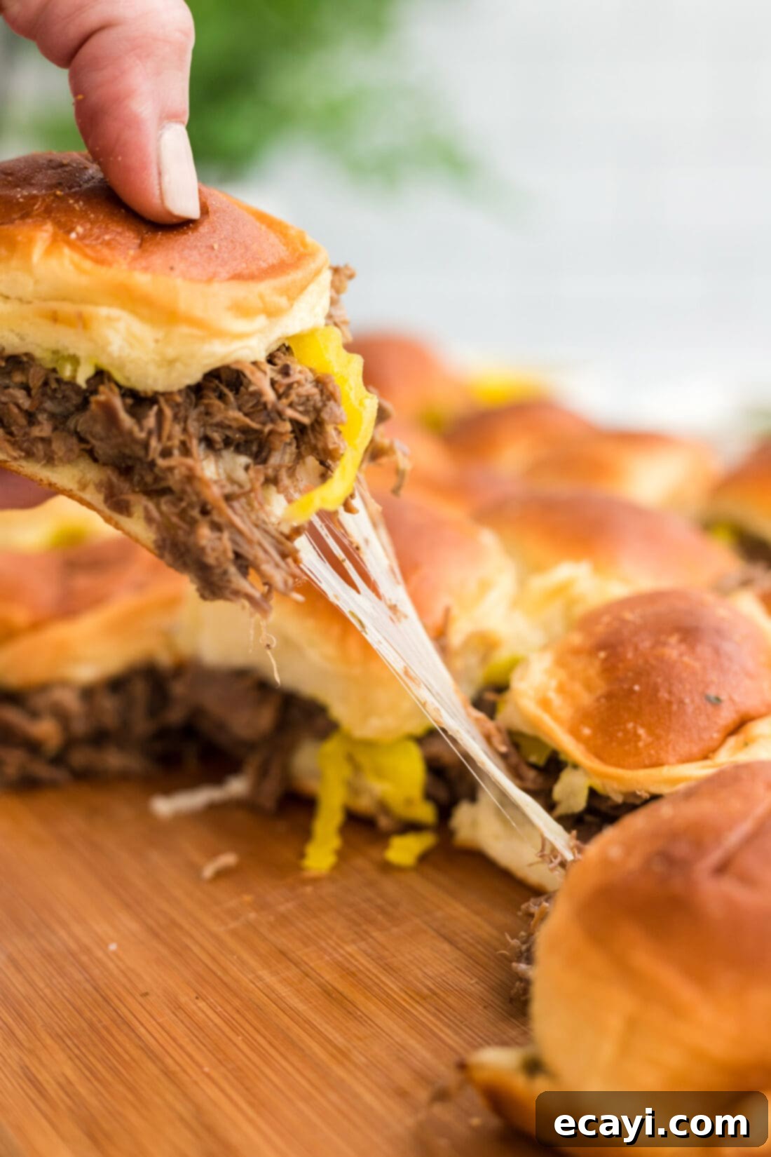 Slow Cooker Mississippi Pot Roast Sliders 3 A hand lifting a golden-brown Mississippi Pot Roast Slider from a baking pan, showing the melted cheese and shredded beef.
