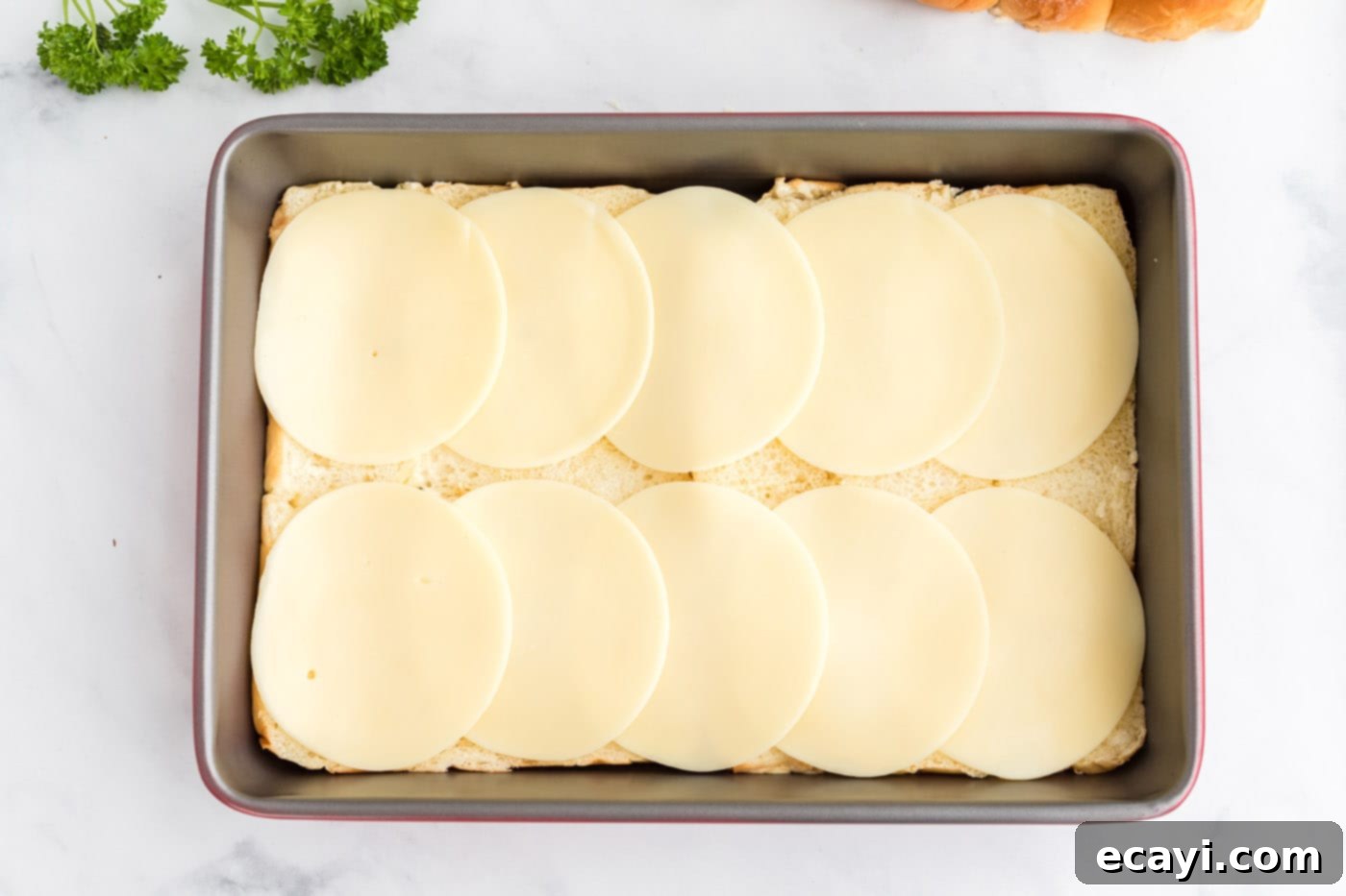 Slow Cooker Mississippi Pot Roast Sliders 7 Provolone cheese slices laid over the bottom layer of Hawaiian rolls in a pan.