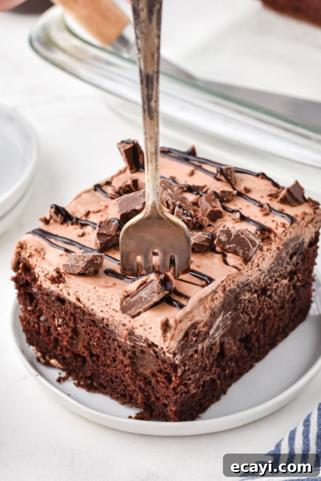 Decadent Chocolate Infusion Cake 12 Slice of triple chocolate poke cake on a plate with a fork, showing layers