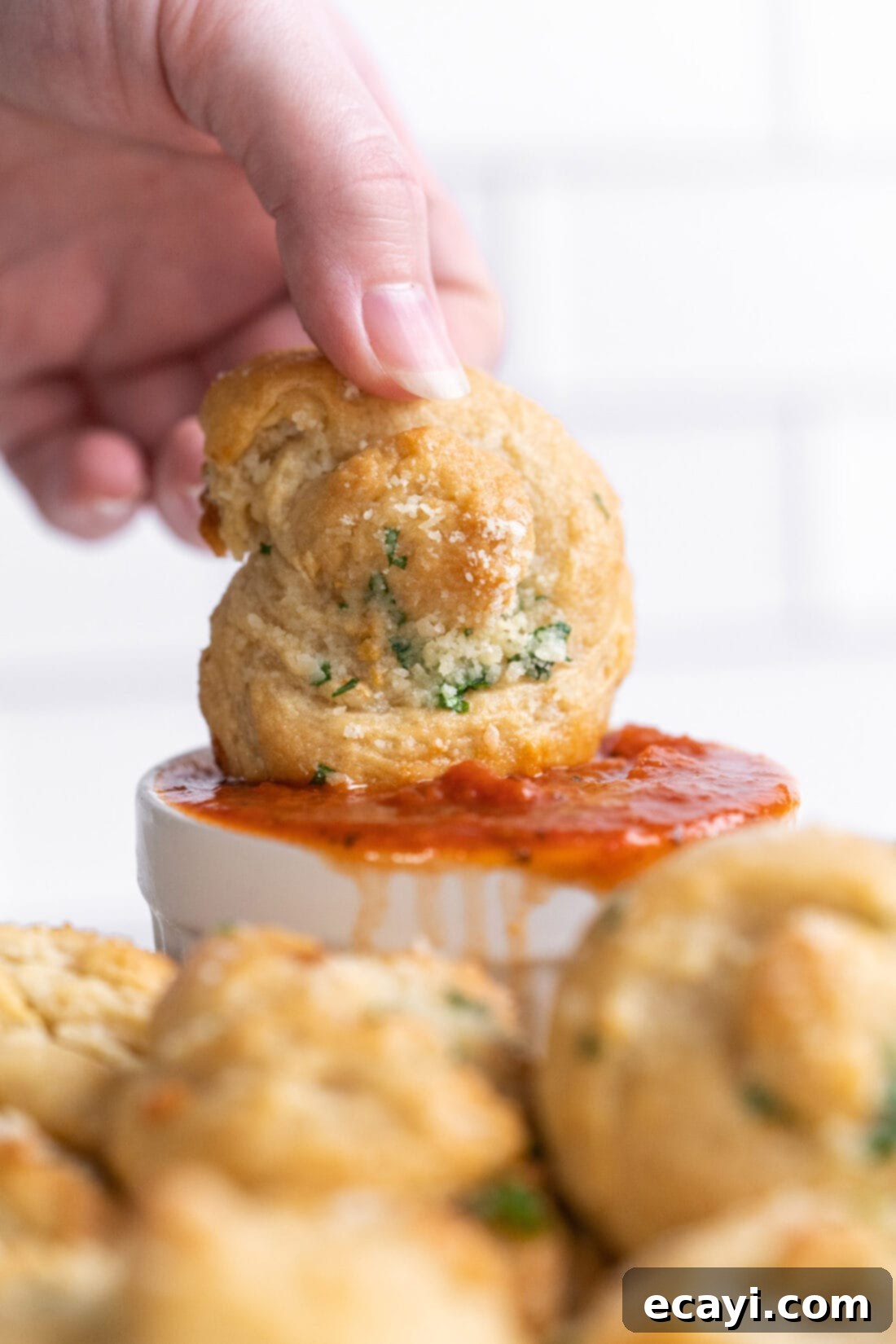 Pillowy Garlic Swirls 2 Dipping a golden, fluffy homemade garlic knot into a bowl of vibrant marinara sauce, showcasing its soft interior and buttery, herby exterior.
