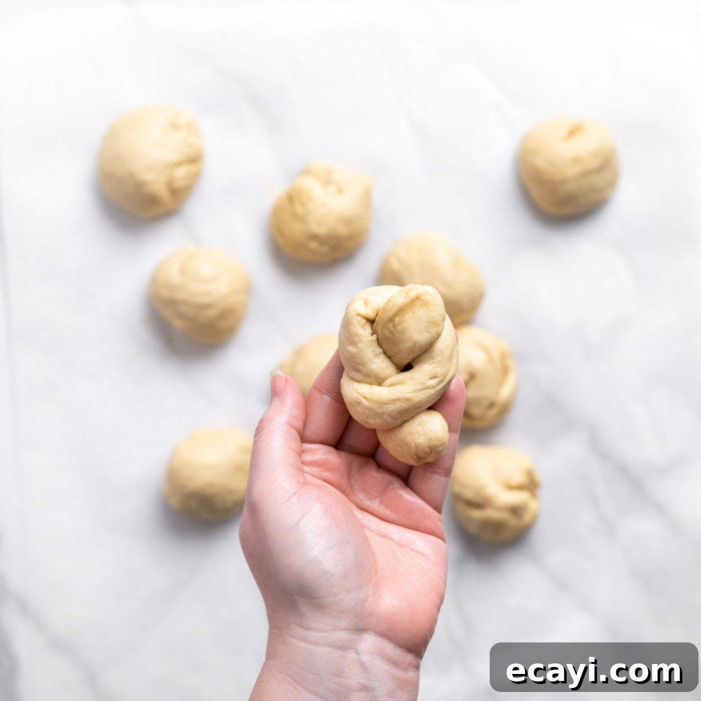Pillowy Garlic Swirls 13 A freshly tied garlic knot dough, showcasing its perfect form, held delicately in a baker's hand before baking.