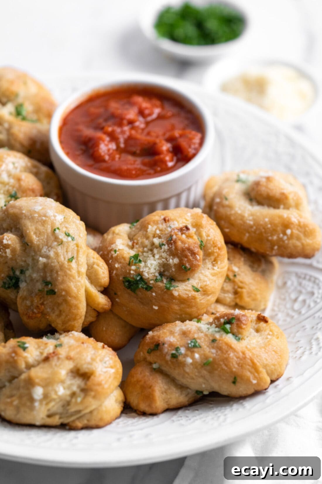 Pillowy Garlic Swirls 3 A plate piled high with golden-brown homemade garlic knots, accompanied by a small bowl of marinara sauce for dipping, ready to be enjoyed.
