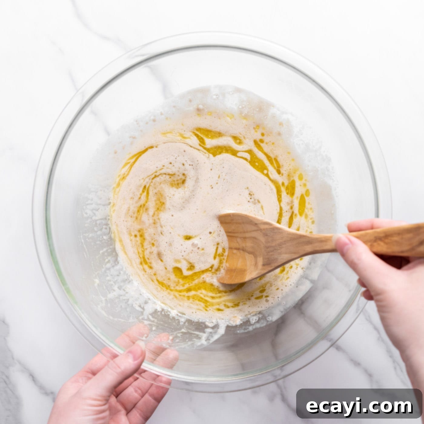 Pillowy Garlic Swirls 6 The liquid ingredients, including sugar, garlic powder, melted butter, olive oil, and salt, being stirred into the activated yeast and water mixture in a large bowl.