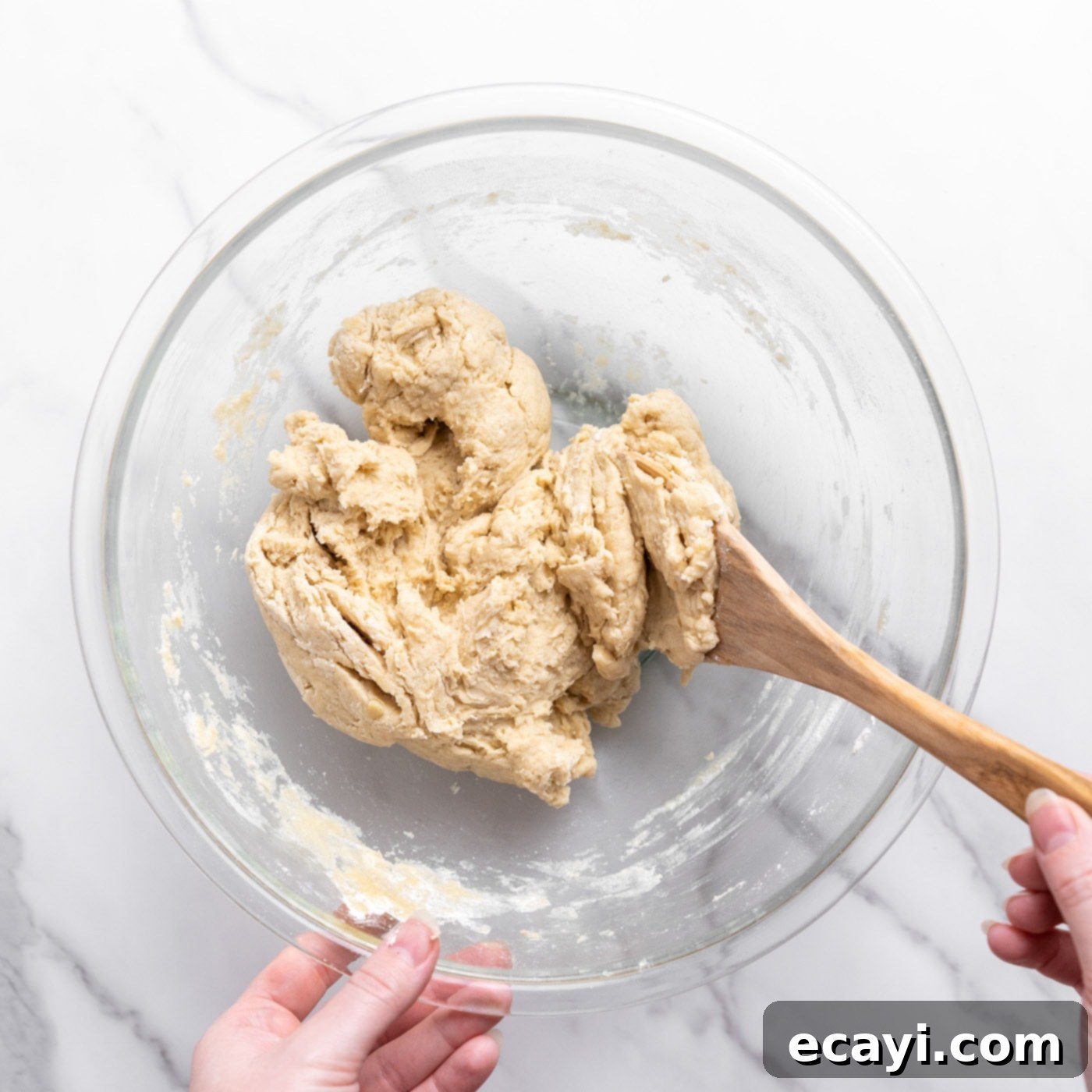 Pillowy Garlic Swirls 7 A shaggy bread dough in a bowl being mixed with a wooden spoon, illustrating the initial stages of dough formation before kneading.