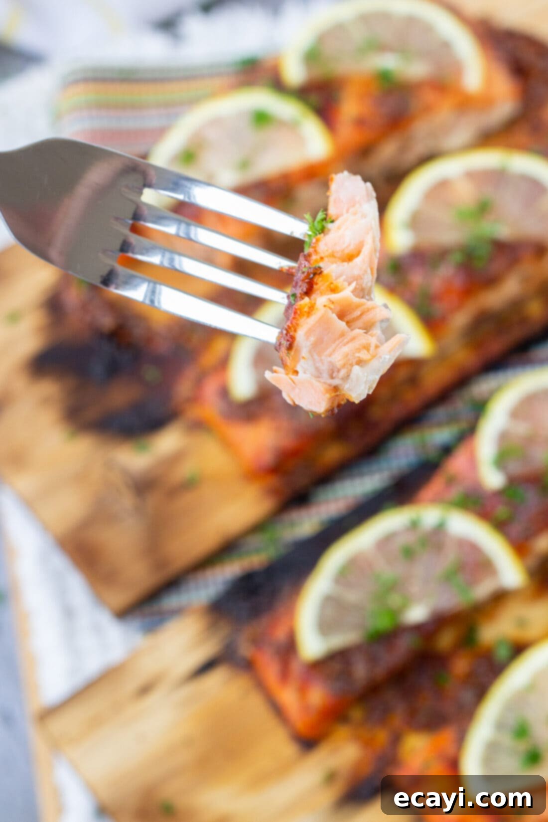 Smoky Cedar Plank Salmon 10 Close up of a fork flaking tender Cedar Plank Salmon, garnished with fresh herbs and lemon