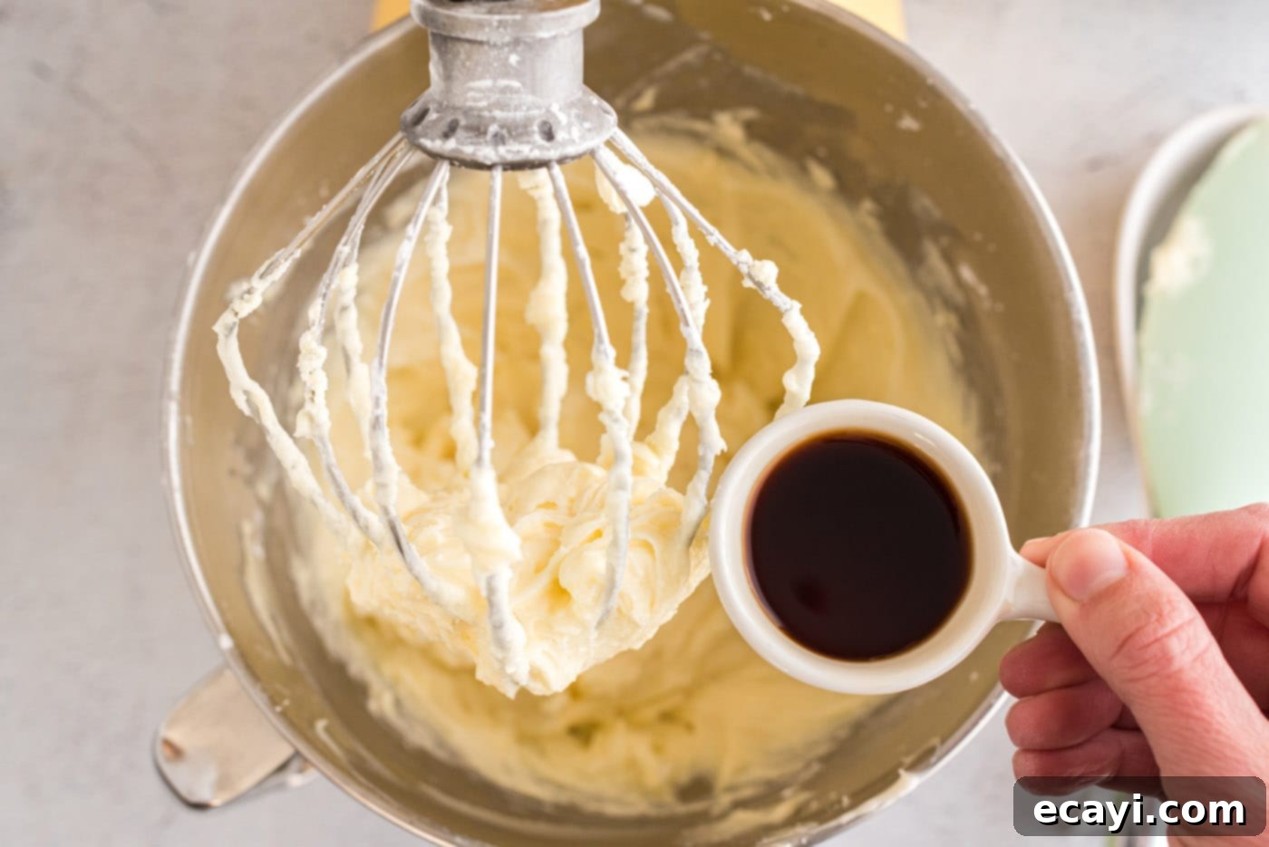 Luscious Cream Cheese Frosting 7 Pouring vanilla extract into the nearly complete cream cheese frosting mixture in a mixing bowl.