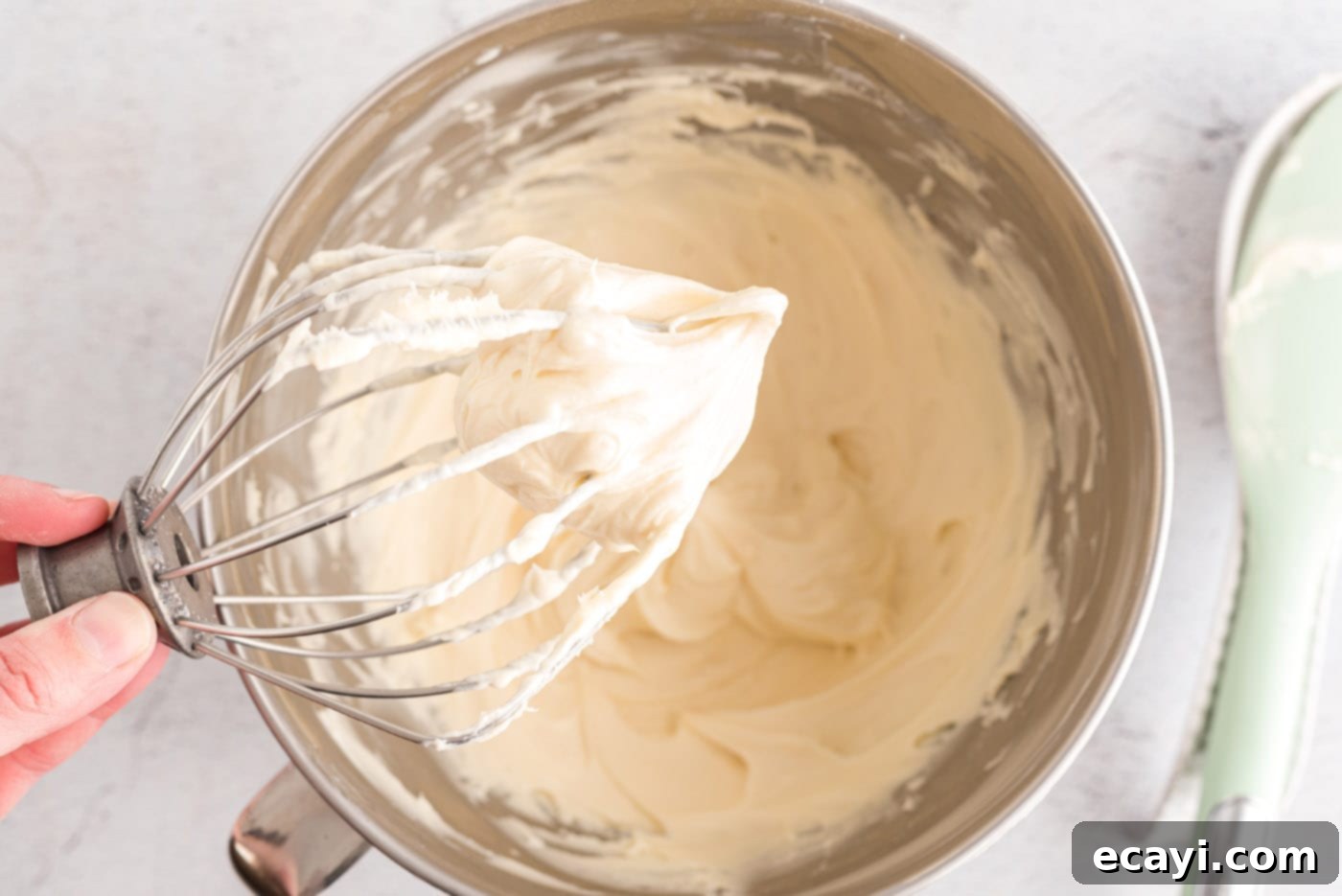 Luscious Cream Cheese Frosting 9 A whisk with freshly made cream cheese frosting clinging to it, indicating the perfect creamy texture.