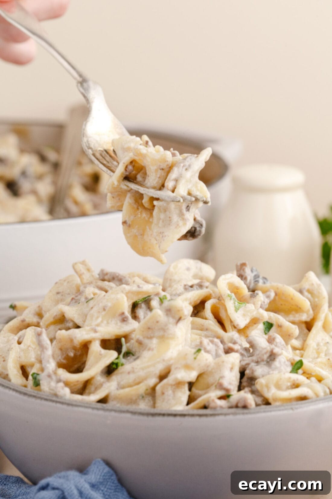 Creamy Ground Beef Stroganoff 3 A fork lifting a portion of creamy Ground Beef Stroganoff with egg noodles and mushrooms from a skillet.