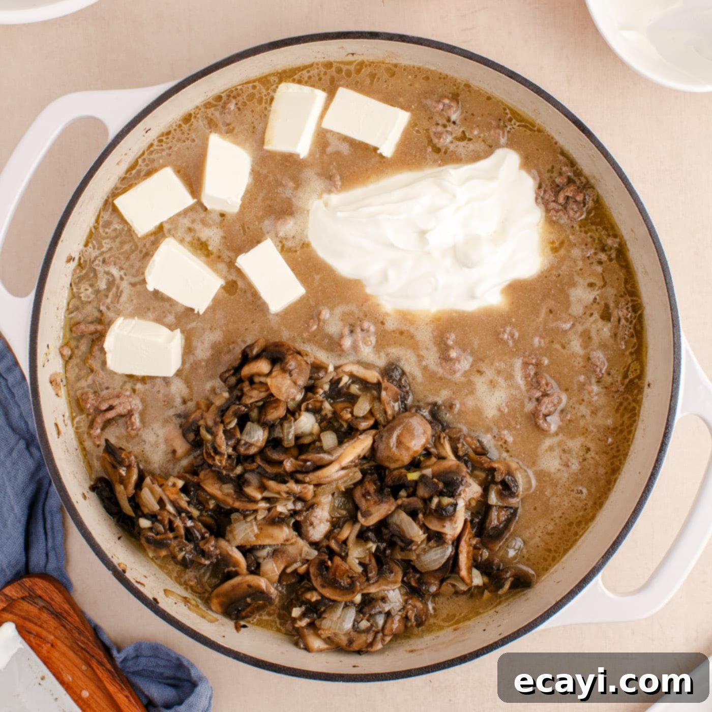 Creamy Ground Beef Stroganoff 9 Mushrooms, sour cream, and cream cheese being stirred into the ground beef stroganoff sauce.