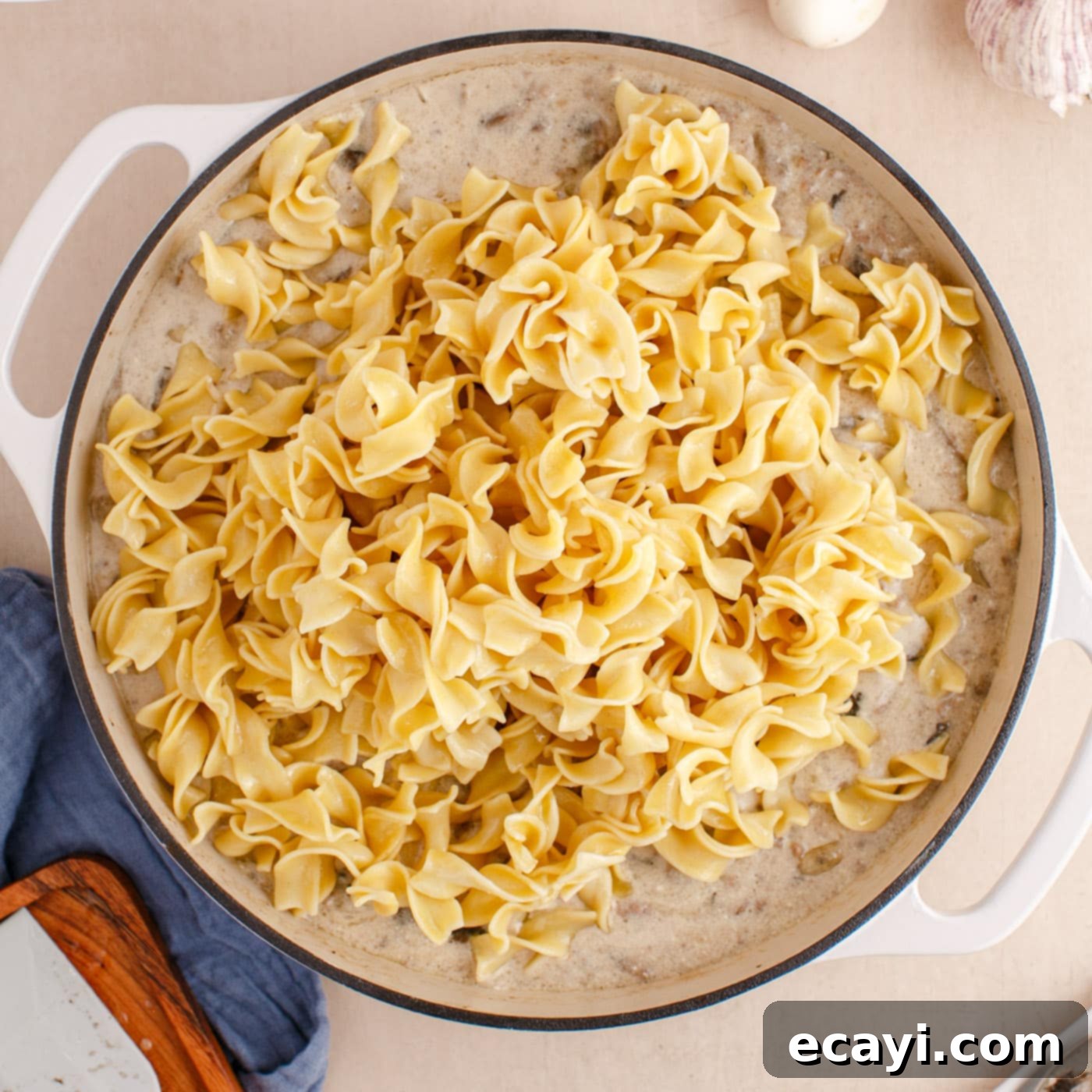 Creamy Ground Beef Stroganoff 10 Cooked egg noodles being added on top of the creamy ground beef stroganoff in a skillet.
