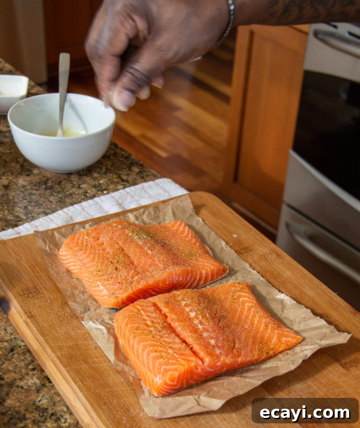 Lemony Salmon 5 Chef sprinkling lemon pepper and garlic salt evenly over salmon fillets before marinating, preparing them for a burst of flavor.