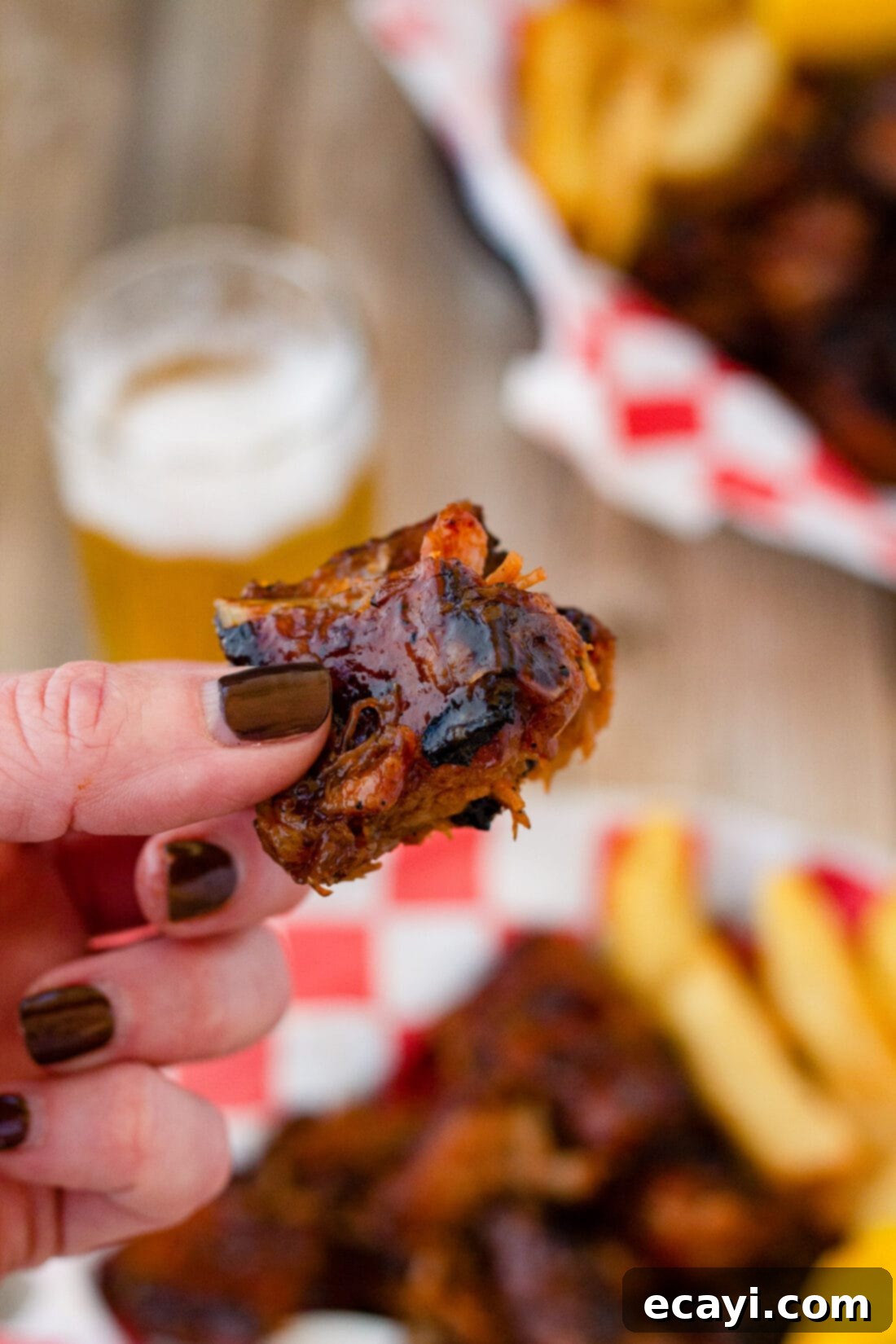 Smoked Rib Ends 8 A hand holding a perfectly sauced and grilled rib tip, highlighting its tenderness and sticky glaze.