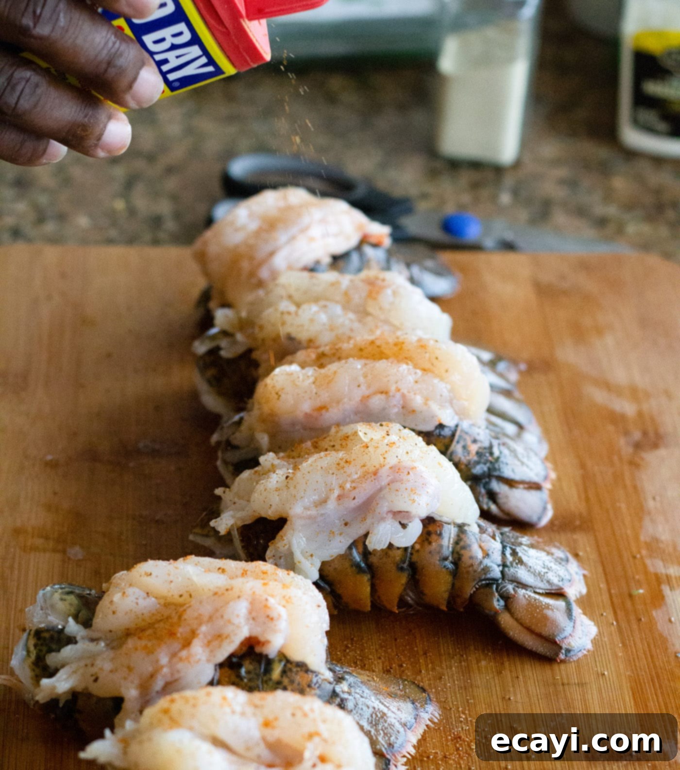 Signature Lobster Roll 6 Seasoning raw lobster tails with Old Bay seasoning before cooking.