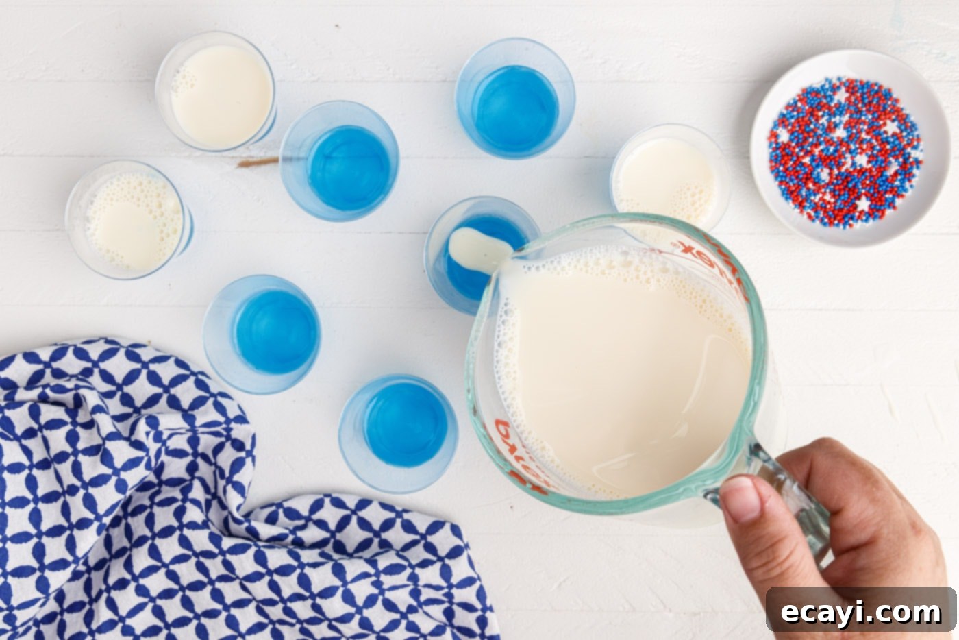 Star-Spangled Gelatin Shots 9 pouring sweetened condensed milk jelly on top of blue jello