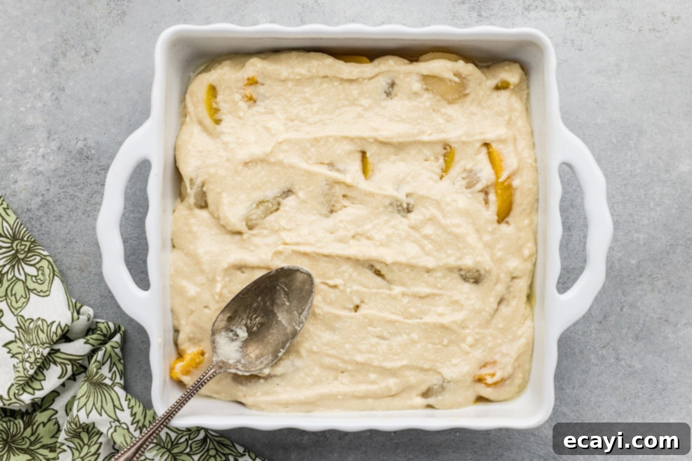 Golden Pear Peach Cobbler 8 spoon spreading out cobbler batter on top of peaches and pears in a baking dish