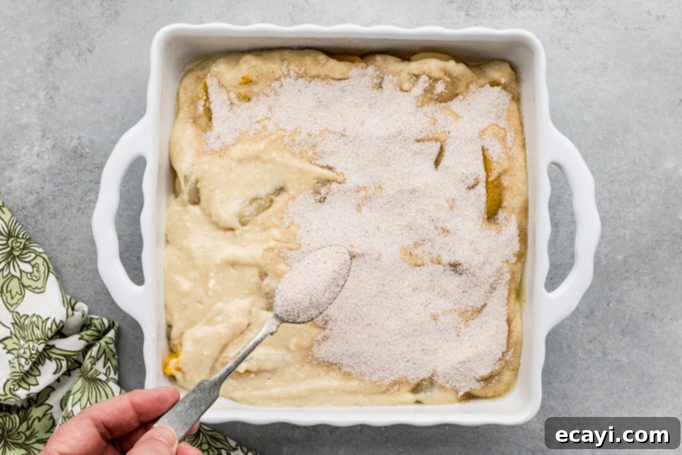 Golden Pear Peach Cobbler 9 spoon sprinkling on sugar mixture over cobble batter in a dish