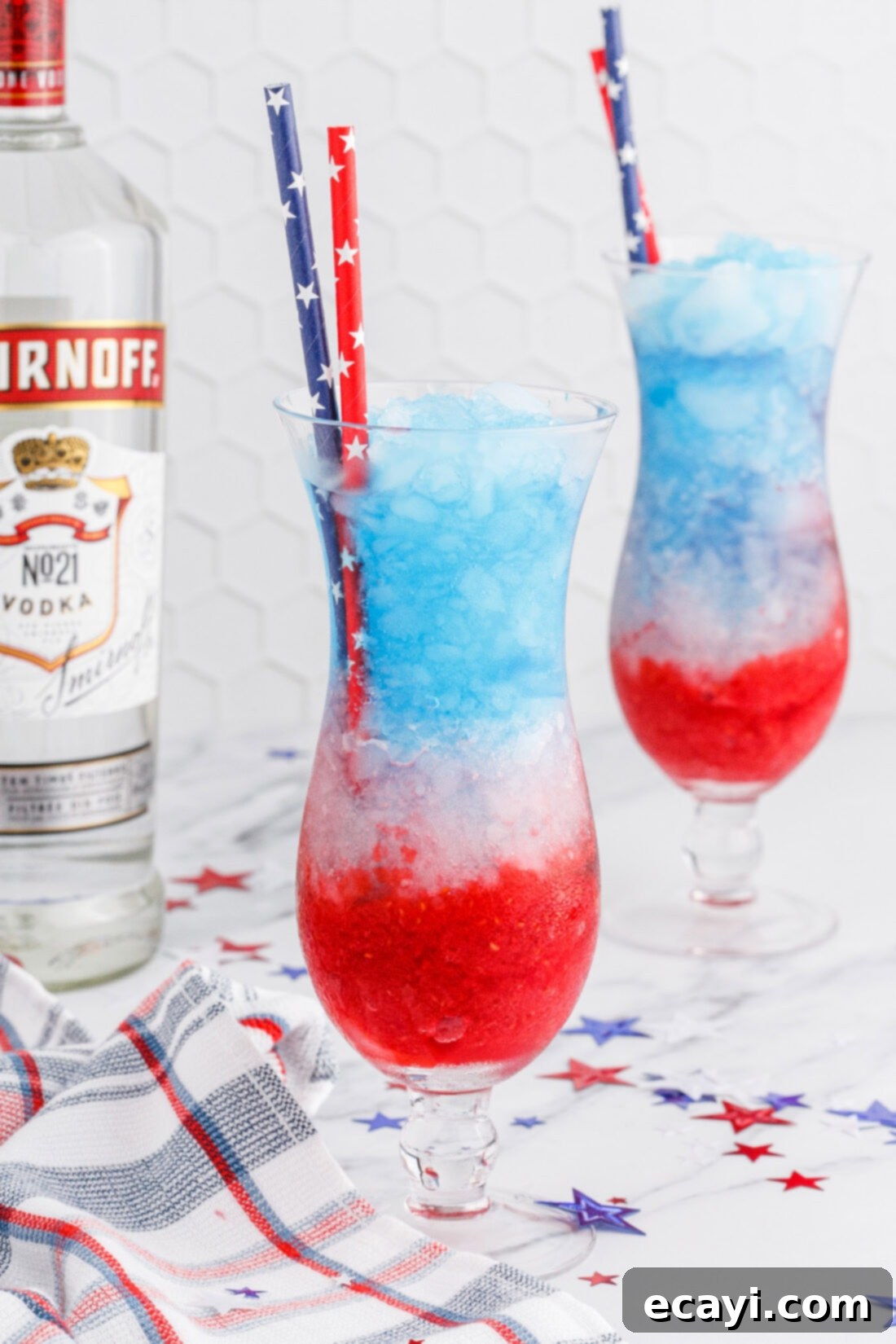 Red White & Boozy Freeze 2 Two glasses of Patriotic Vodka Lemonade Slushie, showcasing the distinct red, white, and blue layers, garnished with fresh raspberries and lemon slices.
