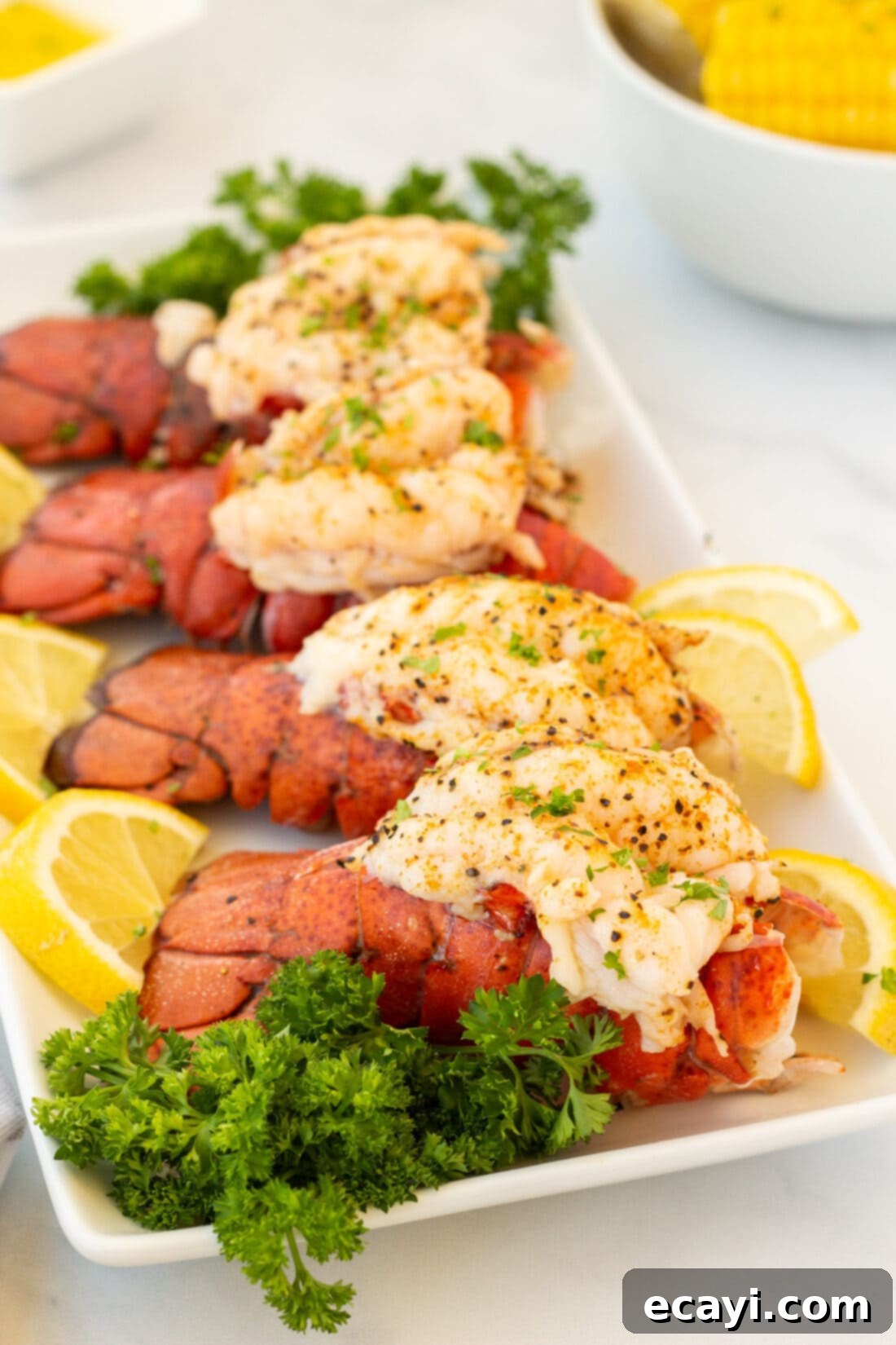 Succulent Steamed Lobster Tail 5 A platter adorned with four beautifully steamed lobster tails, ready to be served, garnished with fresh herbs and lemon wedges.