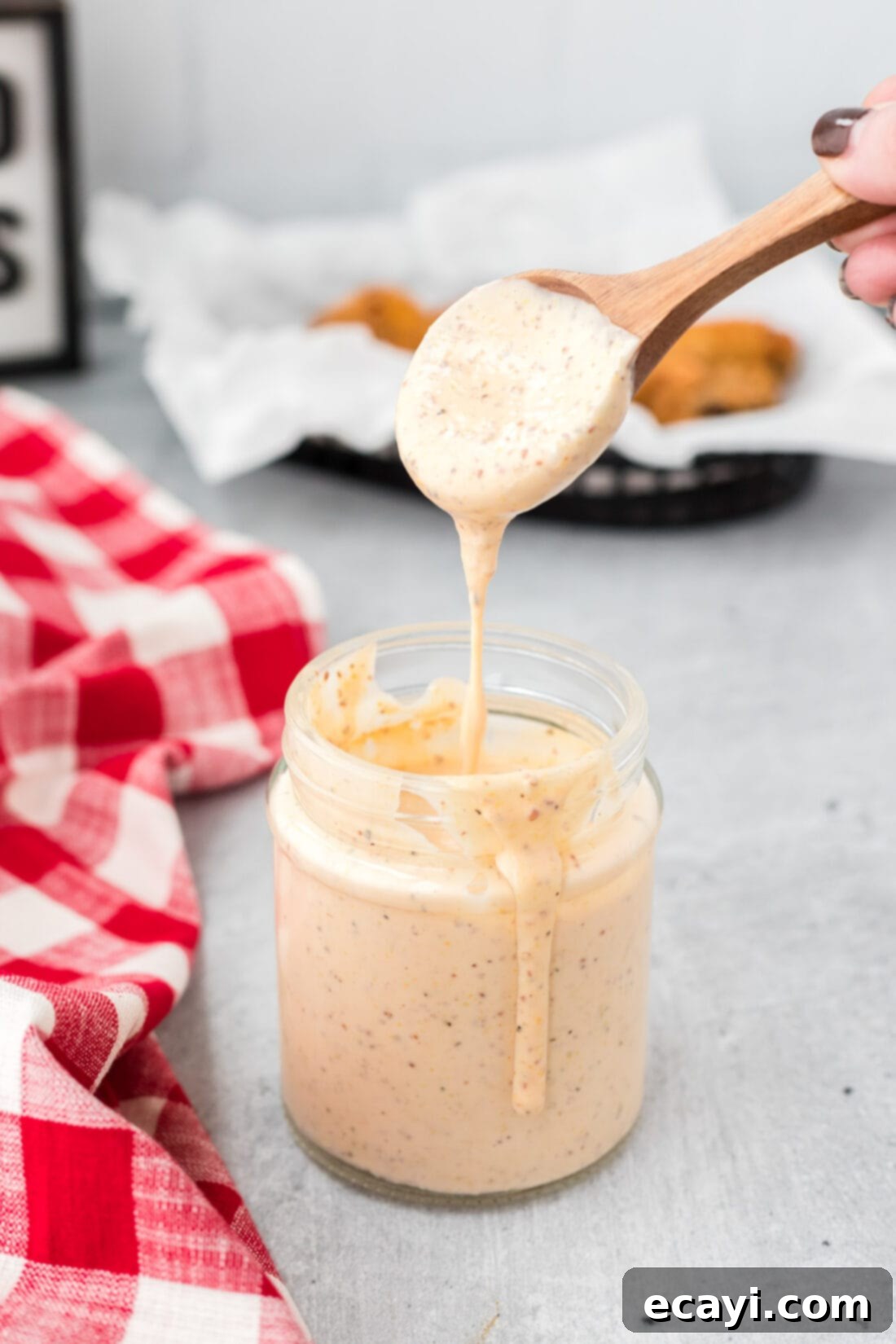 Tangy Southern White BBQ Sauce 2 spoon dripping Alabama White Sauce into jar, showcasing its creamy texture