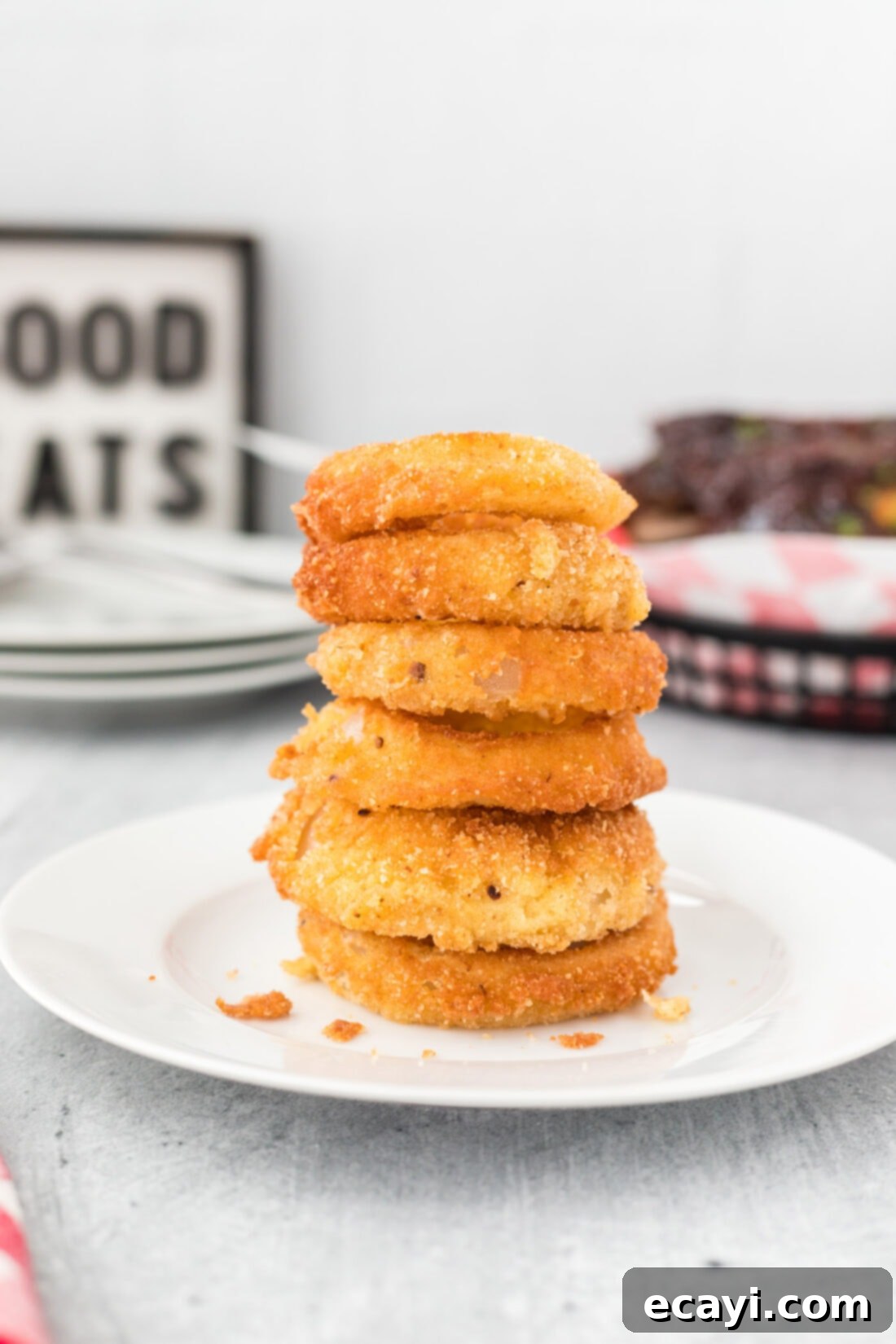 Golden Onion Crisps 12 A tall stack of perfectly fried, golden-brown onion rings on a rustic wooden surface