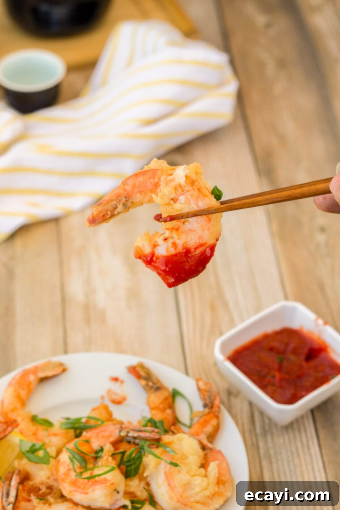 Golden Crispy Shrimp 11 A hand holding a single perfectly crispy shrimp with chopsticks, showcasing its golden color, delicate breading, and inviting texture.