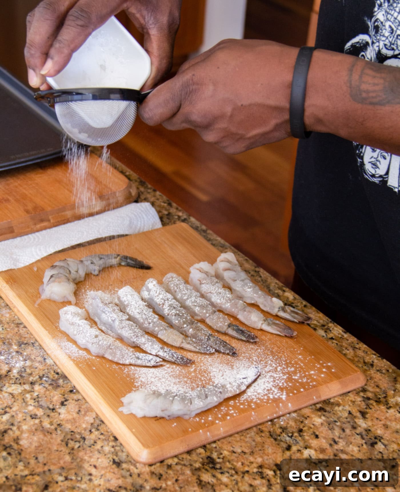 Golden Crispy Shrimp 6 Sifting a fine, even layer of cornstarch over raw shrimp arranged on a cutting board, preparing them for the batter.