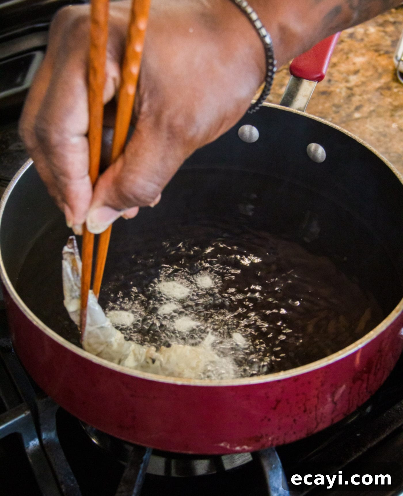 Golden Crispy Shrimp 8 Carefully placing a piece of battered shrimp into hot oil in a skillet for pan-frying to achieve a golden-brown finish.