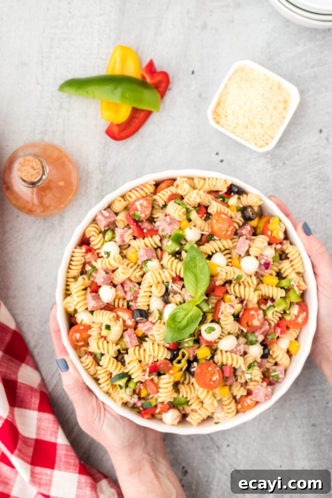 Zesty Italian Pasta Salad 3 Hands serving a portion of vibrant Italian Pasta Salad from a large bowl, highlighting its fresh ingredients.