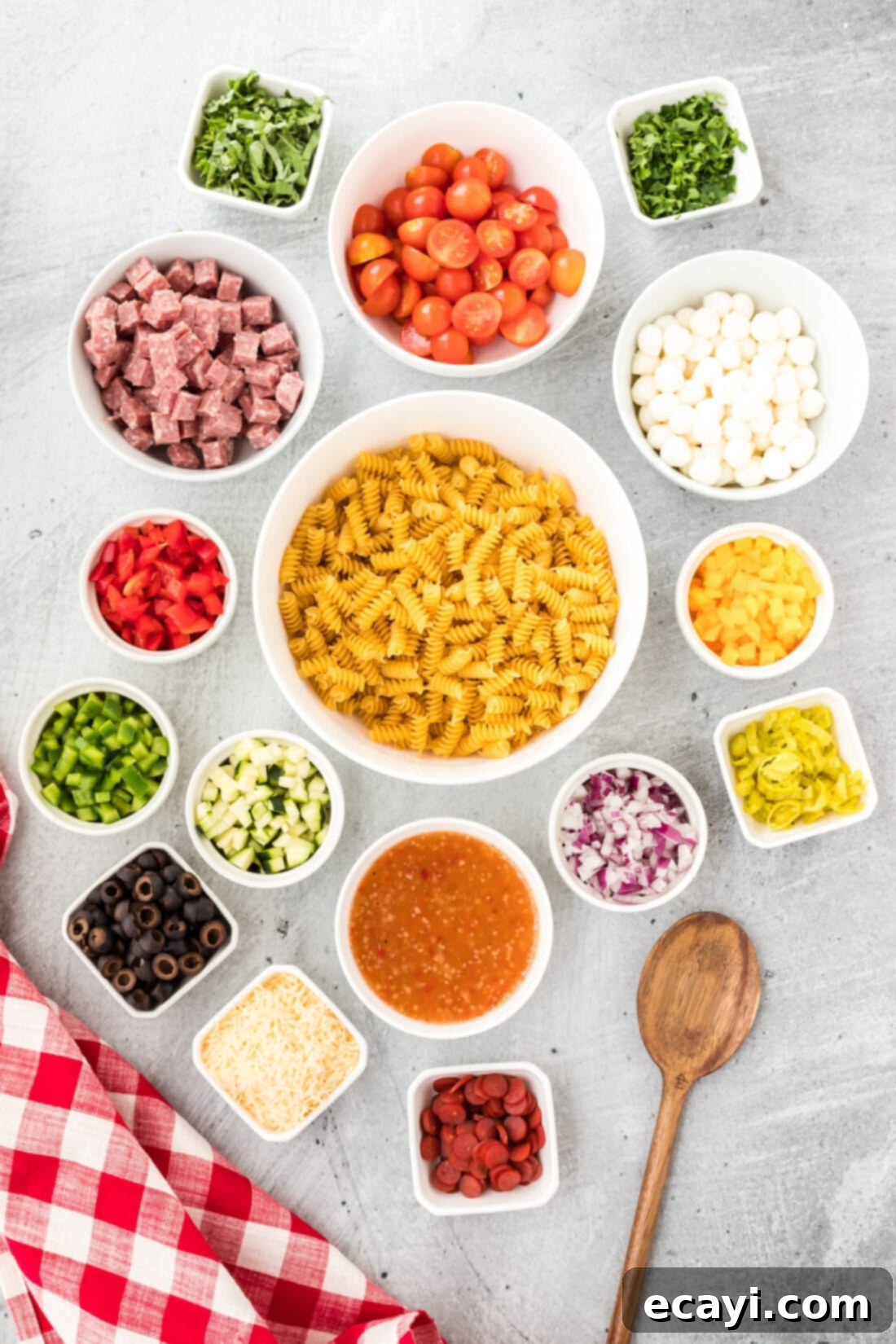 Zesty Italian Pasta Salad 4 Assortment of fresh ingredients for Italian Pasta Salad laid out on a table, including pasta, vegetables, meats, and cheese.