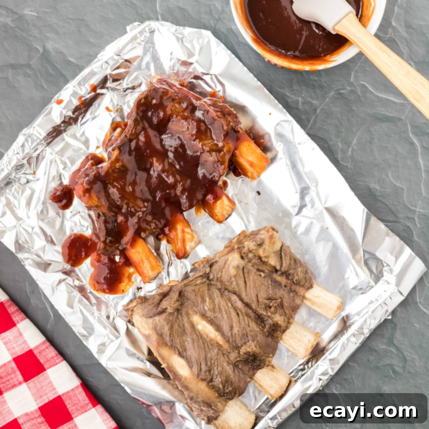 Effortless Instant Pot Beef Ribs 6 A basting brush applying barbecue sauce onto ribs on a baking sheet, preparing them for broiling.