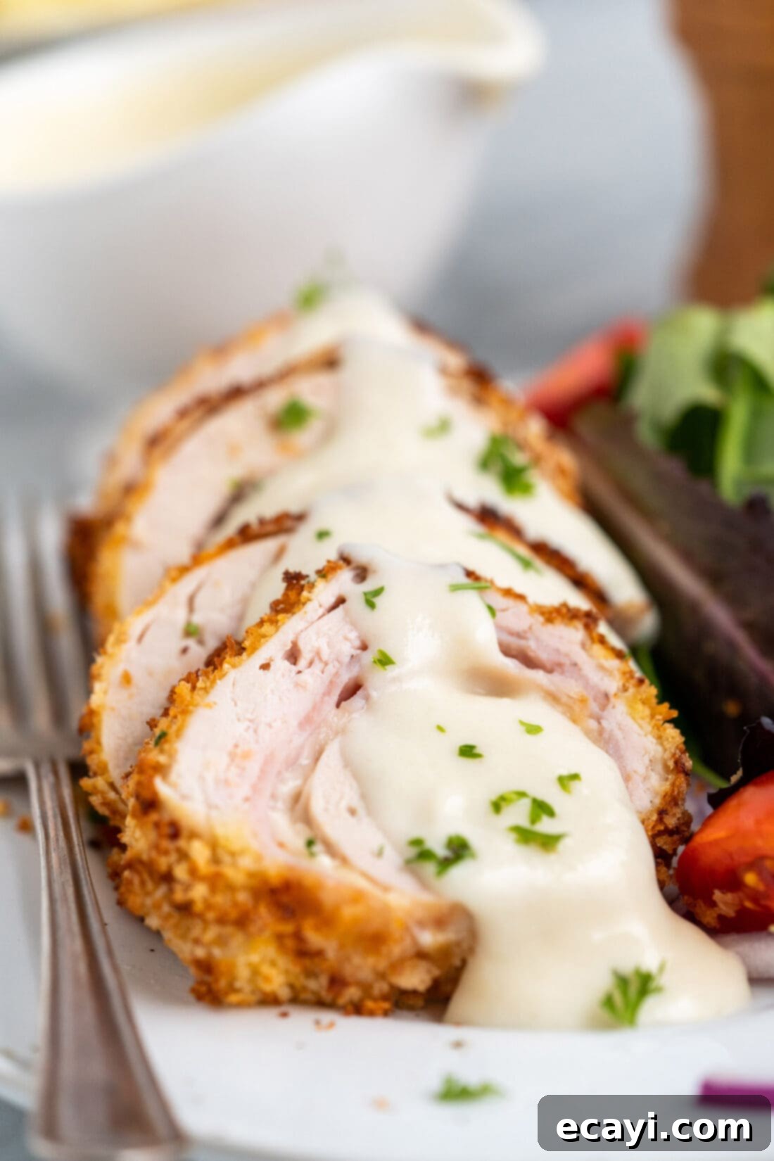 Crispy Air Fryer Chicken Cordon Bleu 3 Sliced air fryer chicken cordon bleu revealing ham and swiss cheese, with a side of creamy dijon sauce