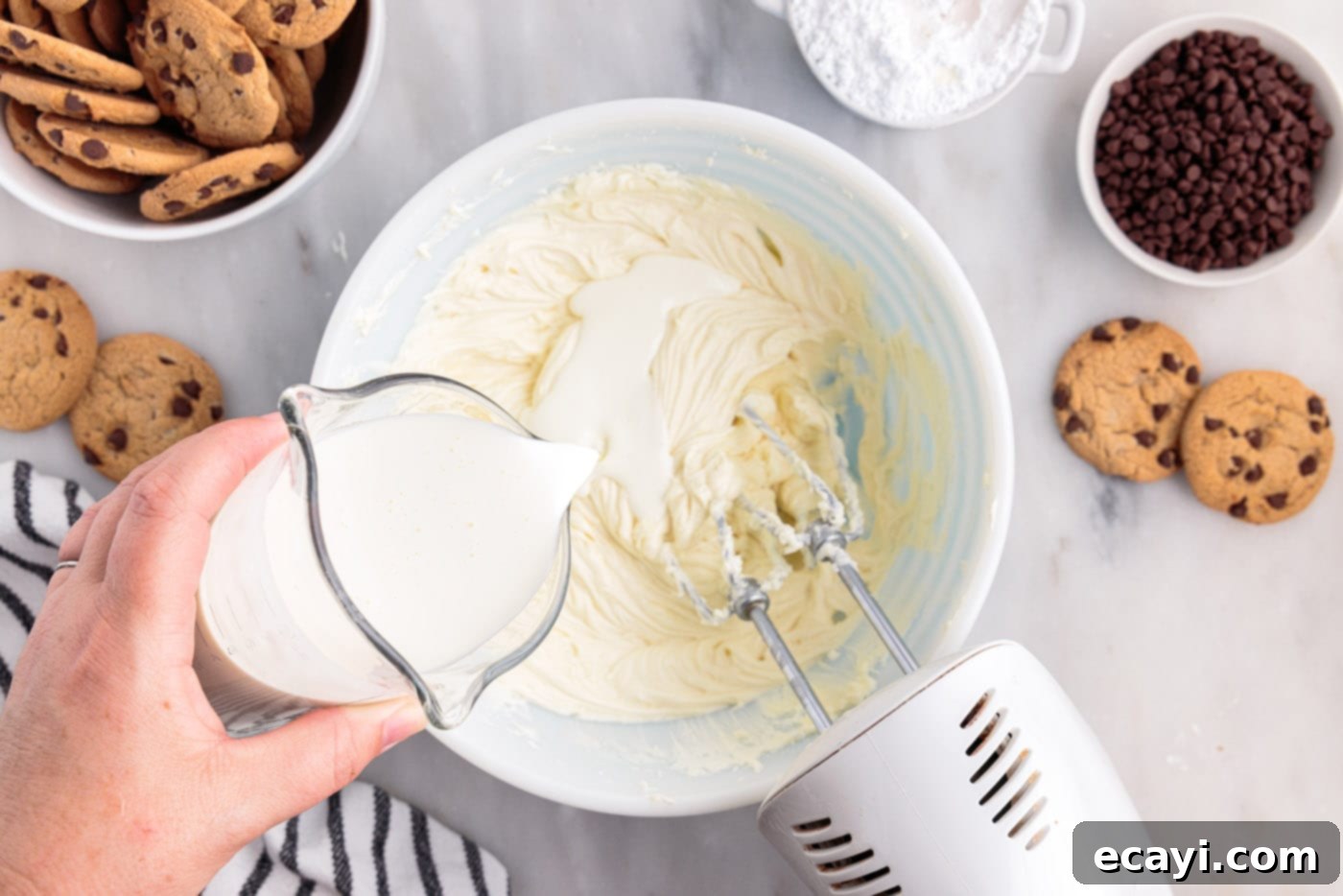 No-Bake Chocolate Chip Cookie Dream Cake 6 Heavy cream being slowly poured into the cream cheese mixture in a bowl while being beaten with a hand mixer.