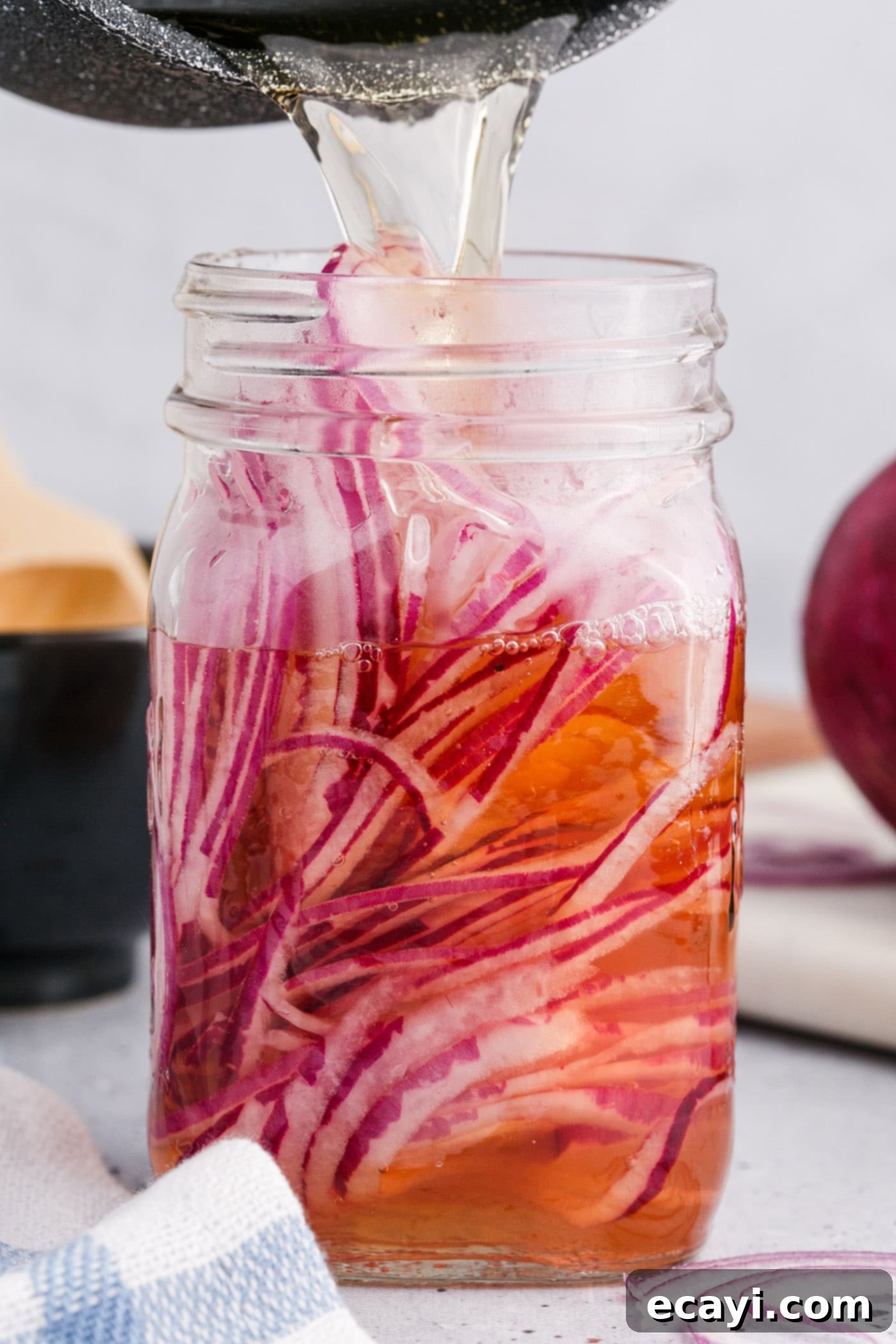 Tangy Pickled Onions 7 pouring vinegar over sliced red onions in a mason jar