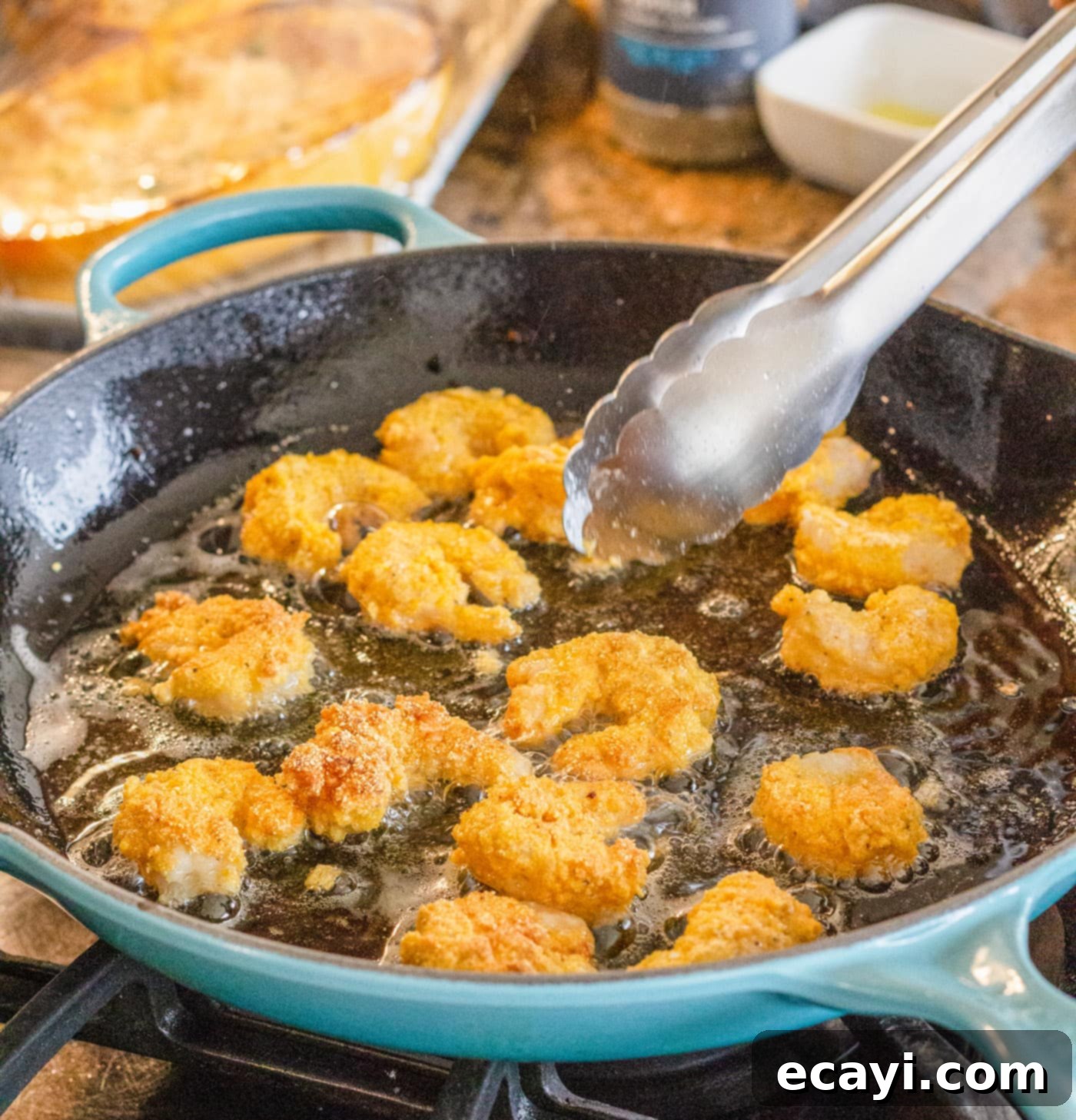 Crispy Golden Shrimp Po' Boy 12 Tongs carefully flipping golden-fried shrimp in a hot skillet, ensuring even cooking.