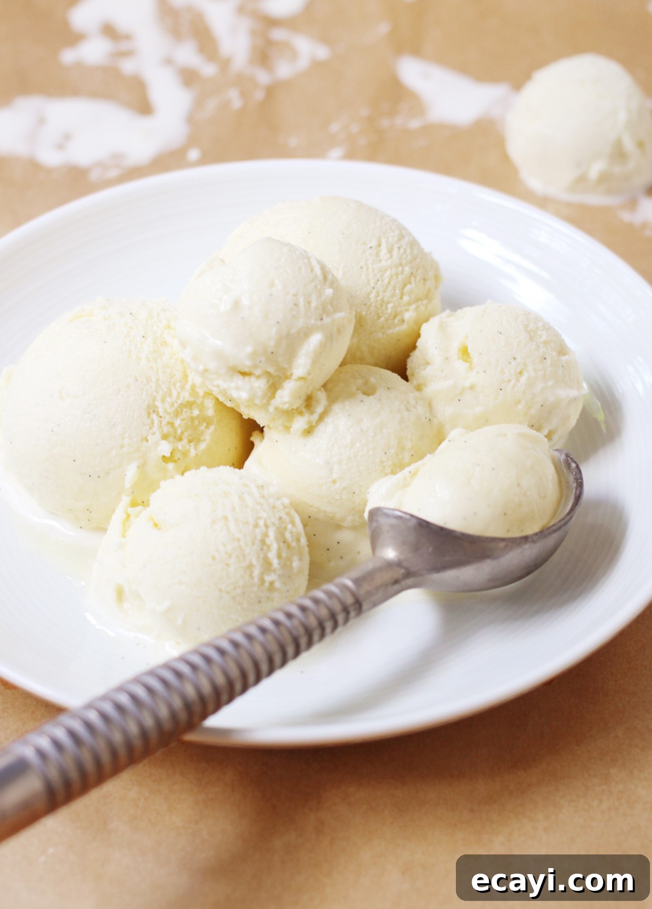 Homemade Italian Gelato: Simple Steps to Sweet Perfection 7 A white plate holds several scoops of Italian ice cream, with one scoop resting in a metal ice cream scooper at the edge. Some melted gelato is visible on the brown surface below. // FoodNouveau.com