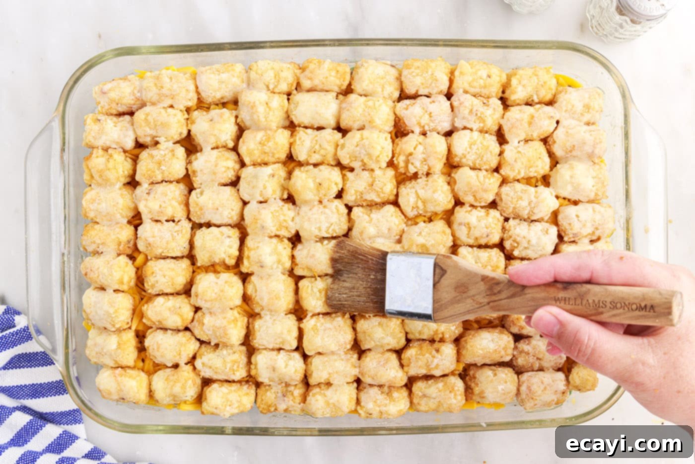 Crispy Tatertot Bake 12 Melted butter being brushed over the frozen tater tots on the casserole