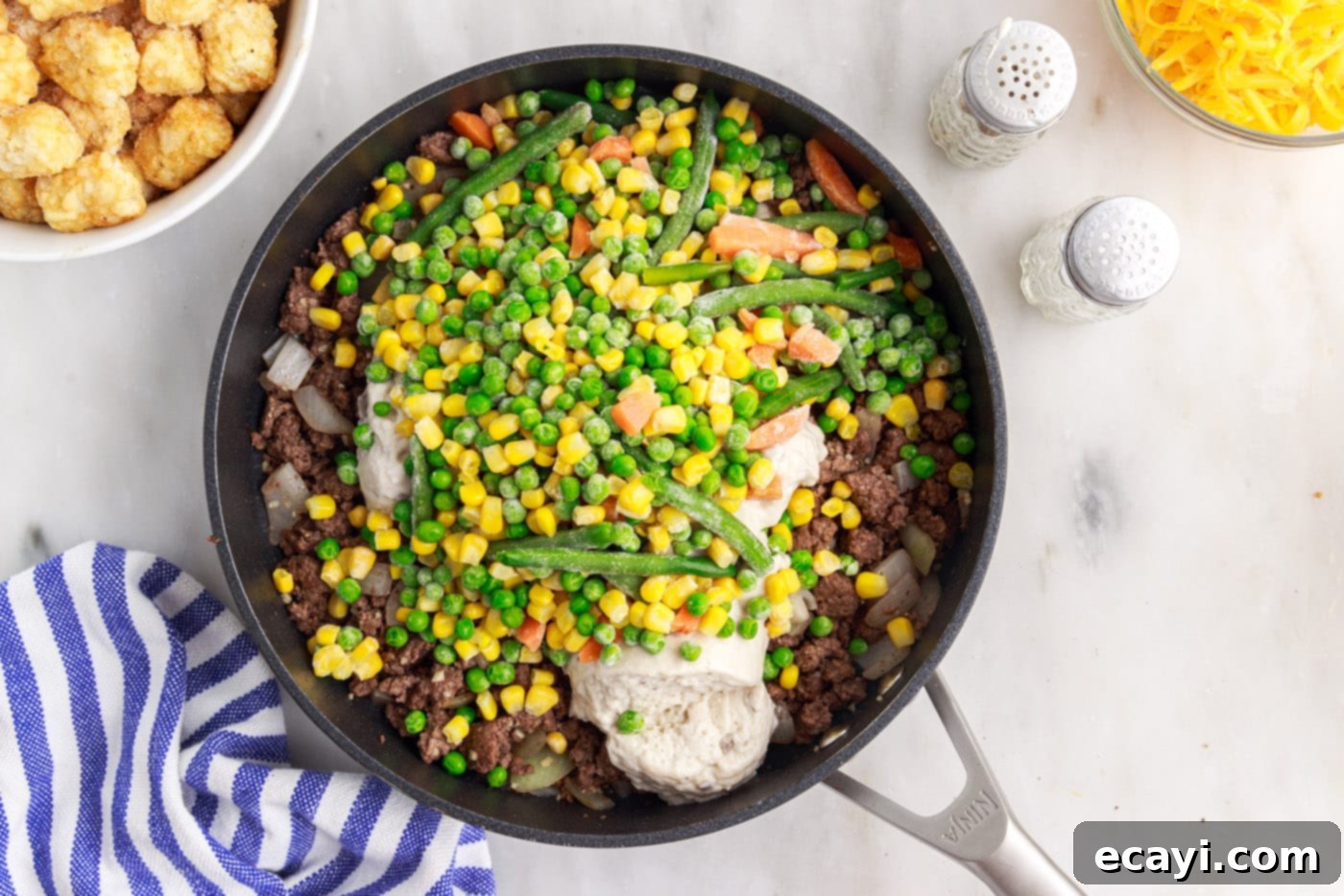 Crispy Tatertot Bake 7 Cream of mushroom soup and frozen mixed vegetables added to the beef mixture in a skillet